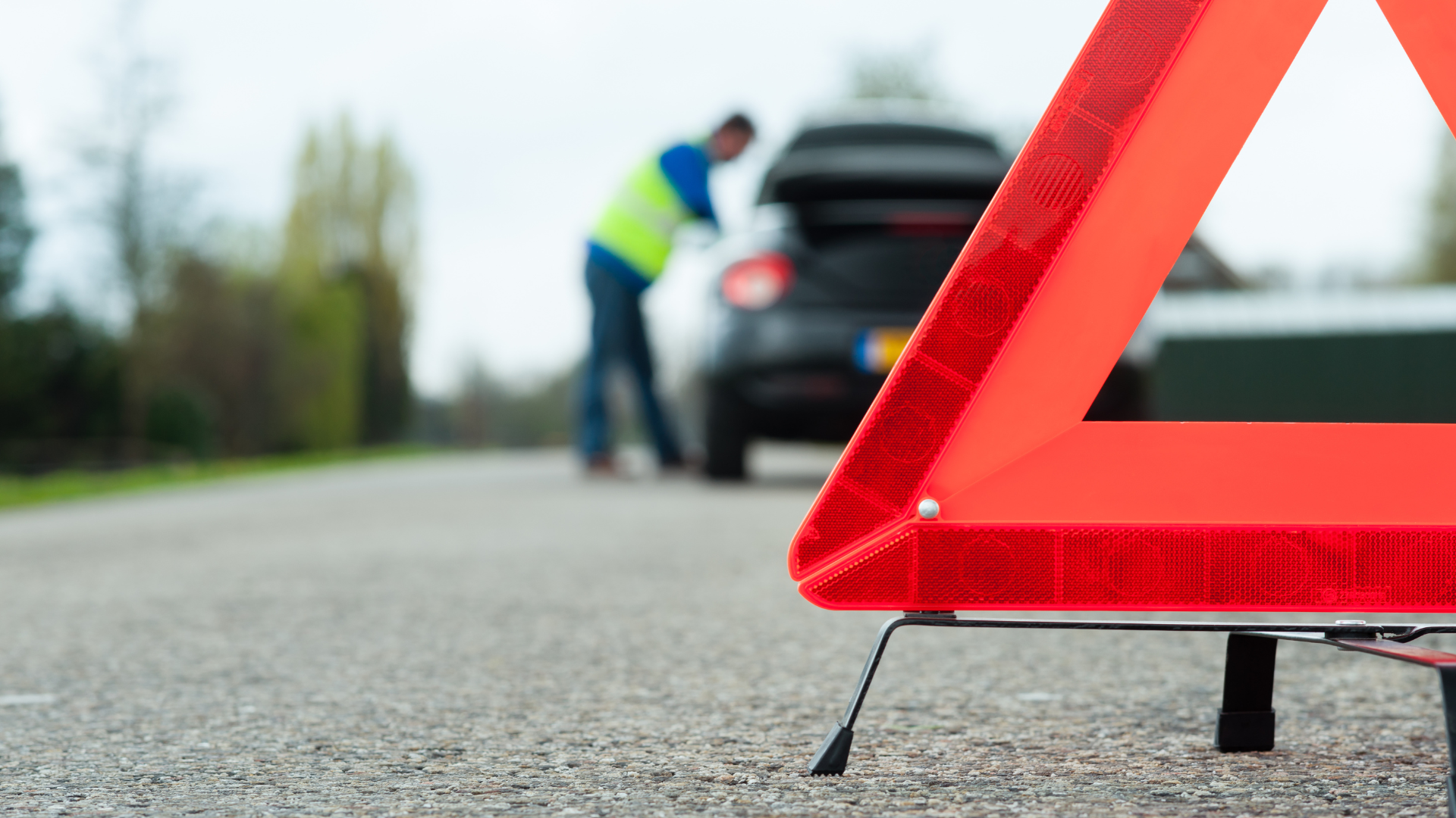 Red warning triangle on road; person by broken-down car.