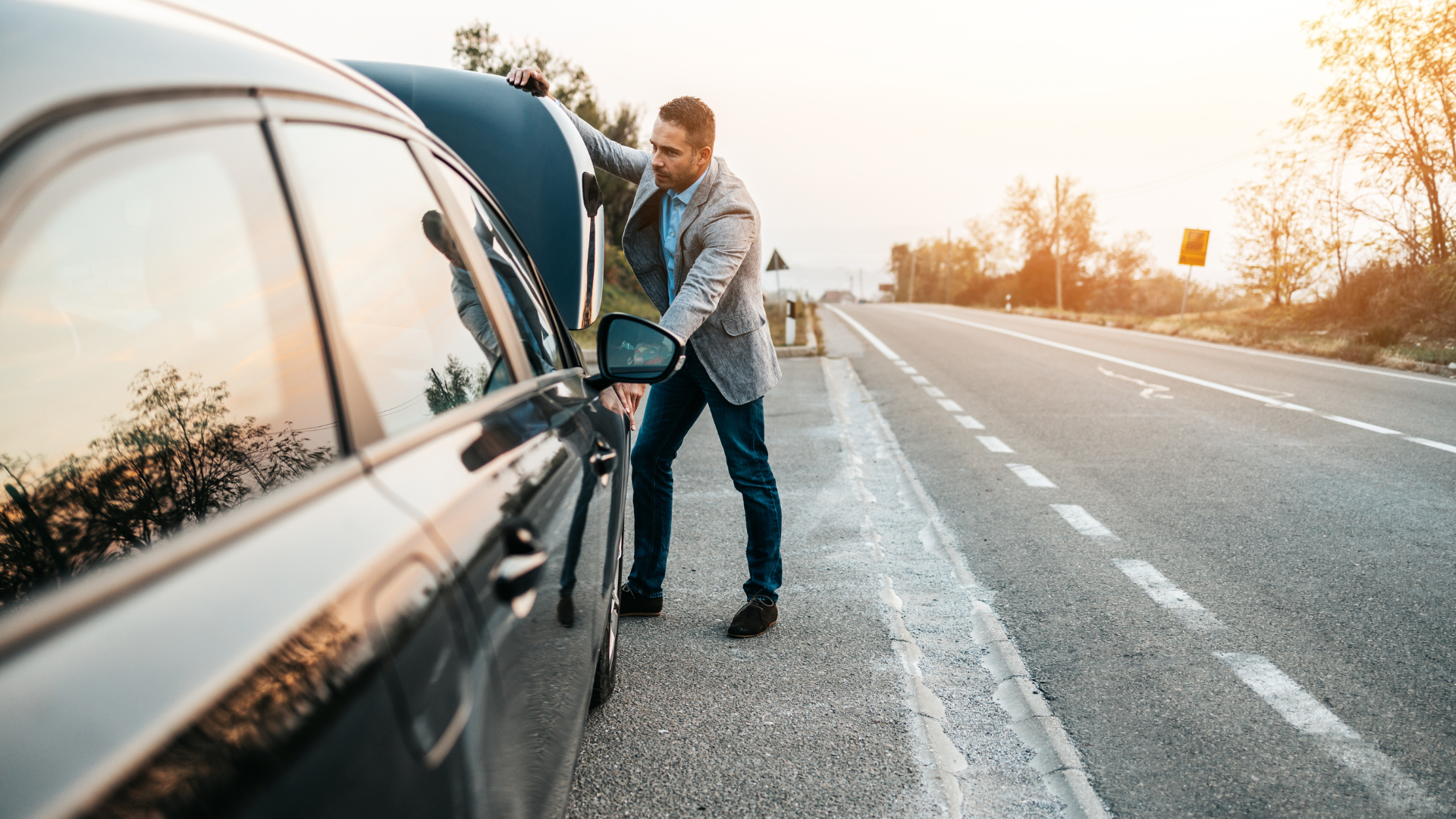 Man with car trouble, standing on roadside, opening hood, late afternoon.