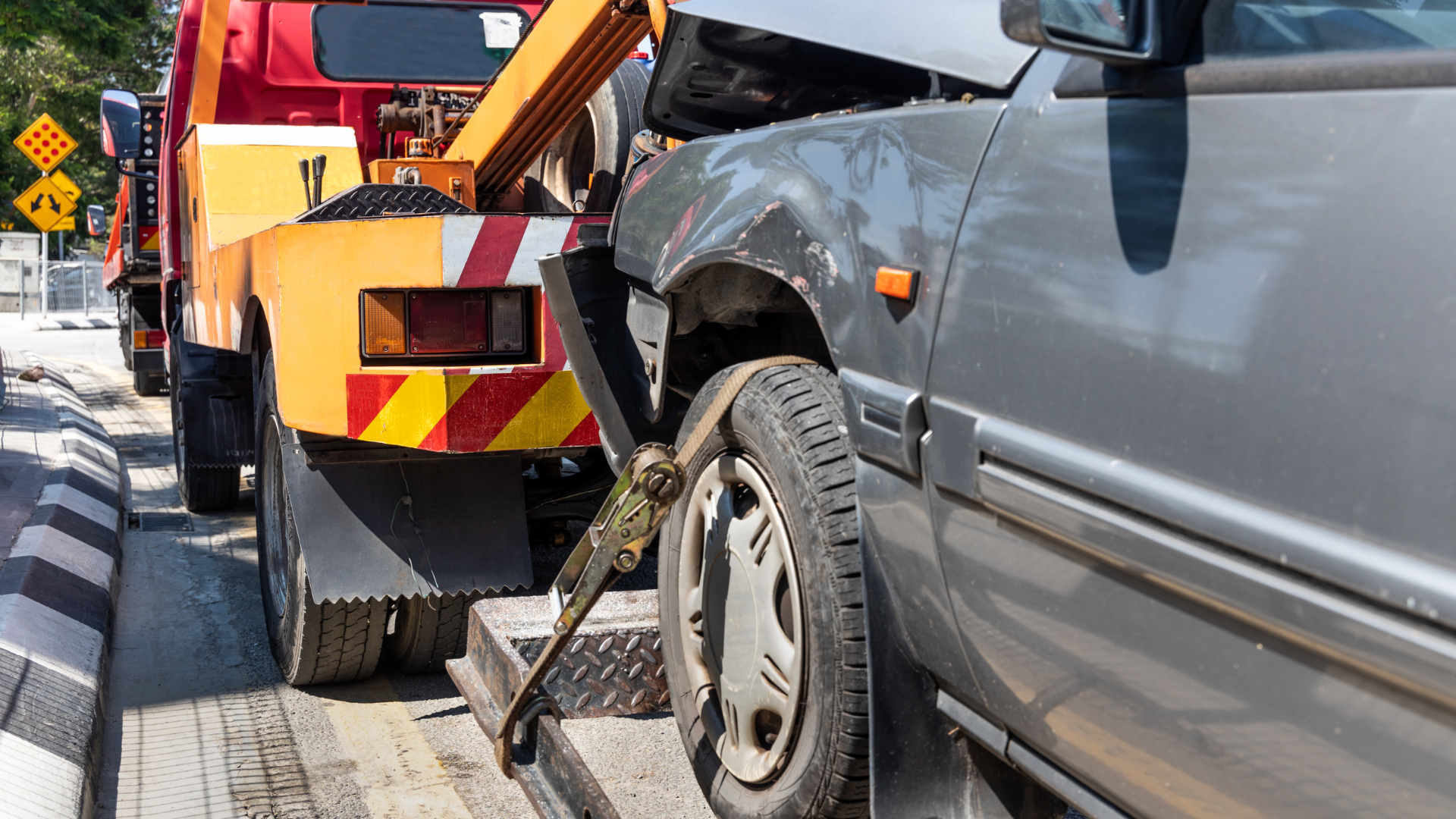 Tow truck loading a damaged gray car onto its flatbed.