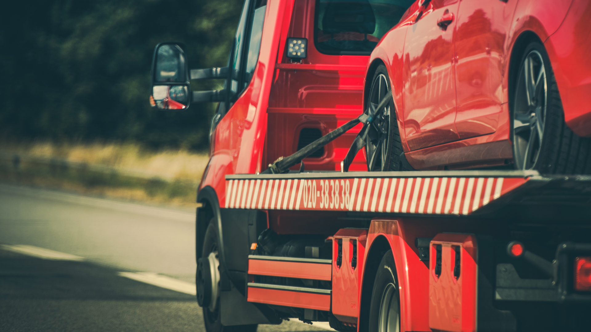 Red tow truck hauling a red car on a highway.