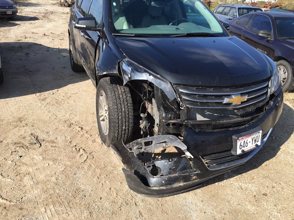 Black Chevrolet SUV with front-end damage; parked on dirt.