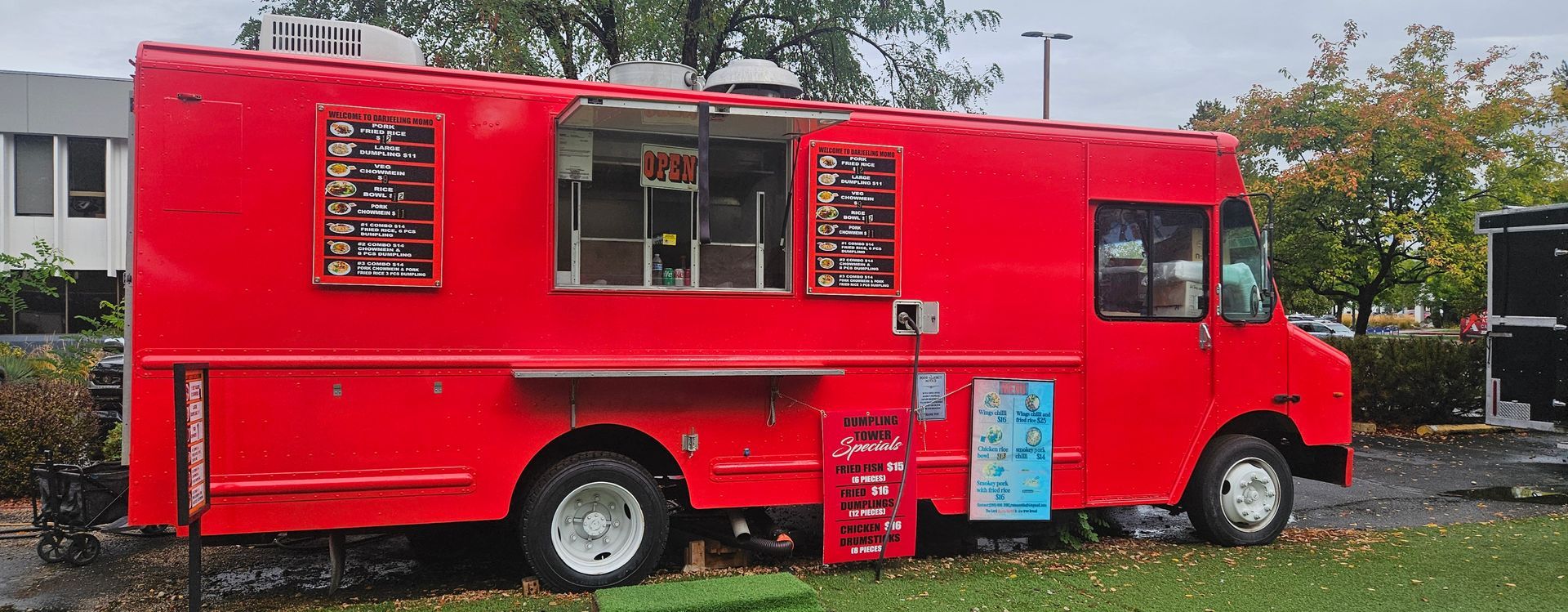 A red food truck with menus and a serving window parked on grass.