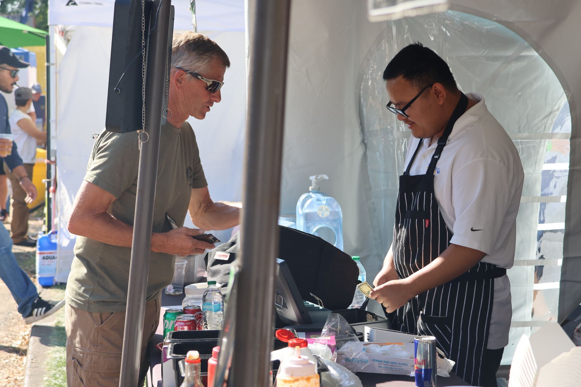 Man ordering food from a chef at an outdoor food stall. They are both focused on the transaction, it's daytime.