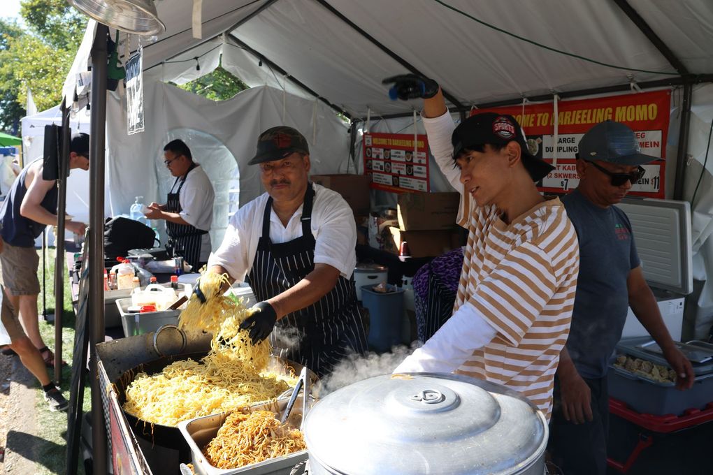 People cook and serve noodles at an outdoor food stall.