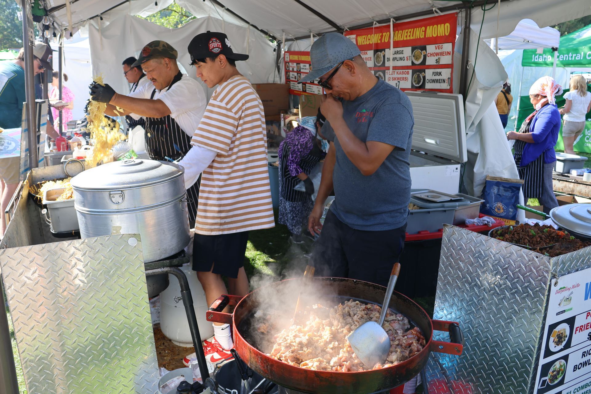 People cooking food at an outdoor food stall, using a large wok.