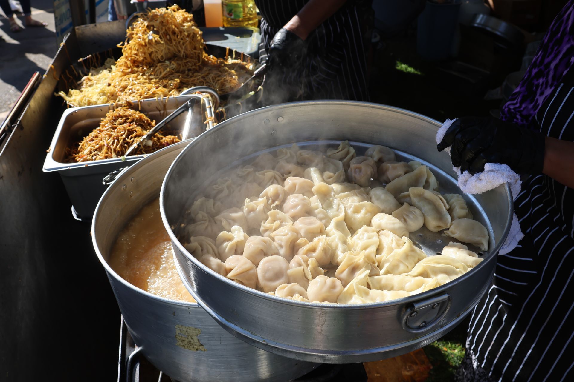 Person holding a steamer basket of dumplings; food stall with noodles.