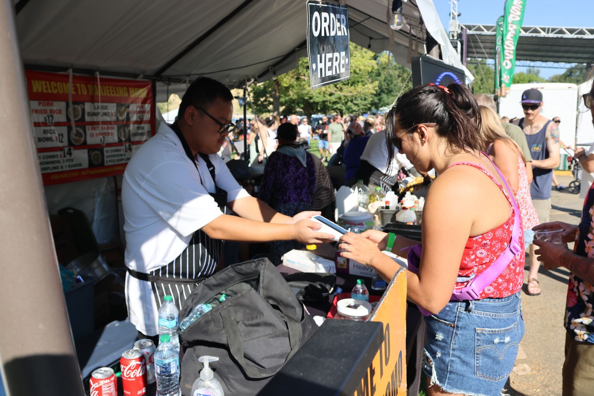 Man serving food to a woman at a food stall. Other people are in the background.
