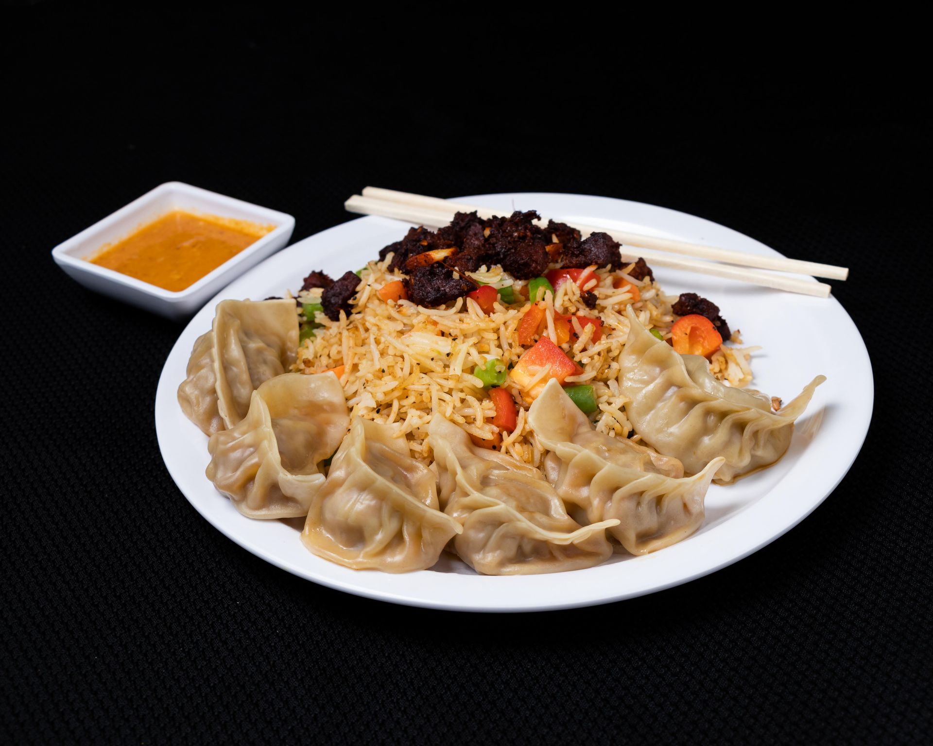 Plate of dumplings, fried rice, and sauce. White plate on black background.