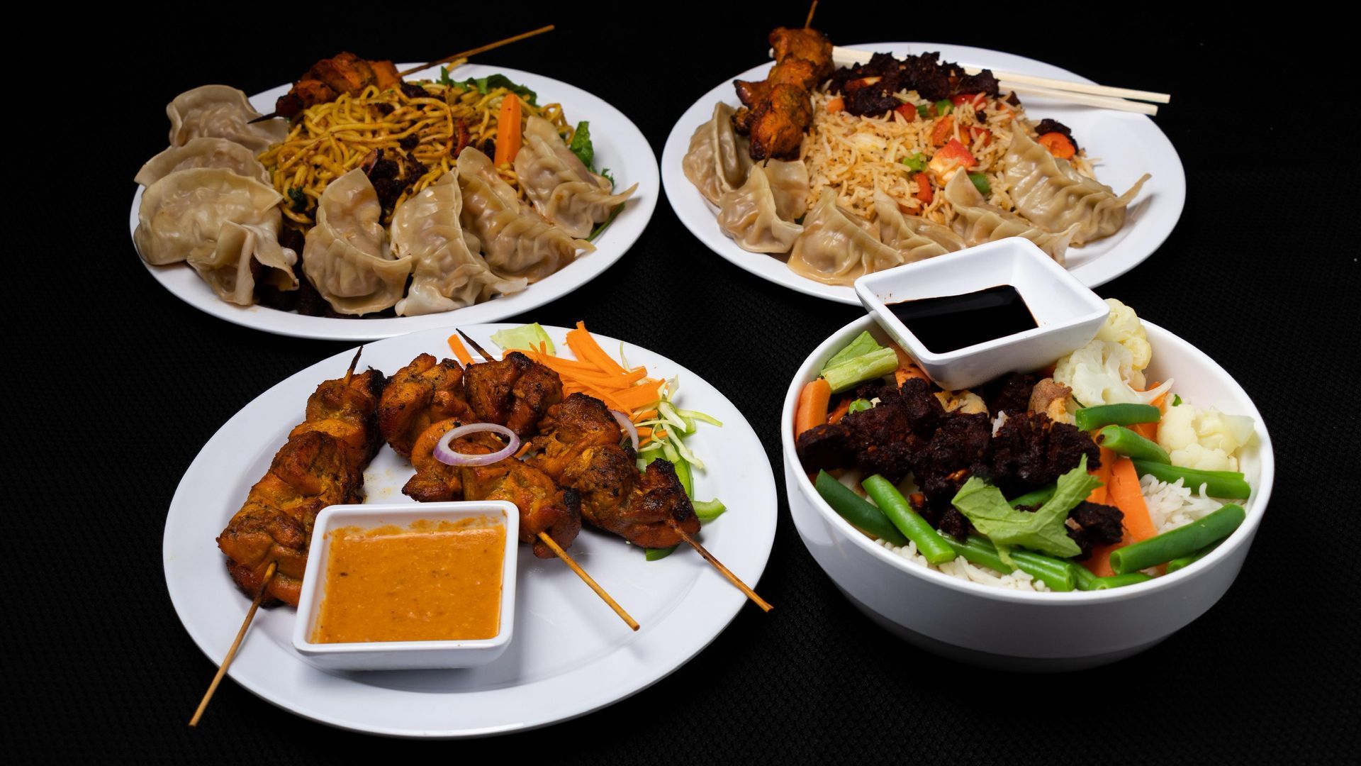 Four plates of Asian food: dumplings, skewers, rice, and veggies.