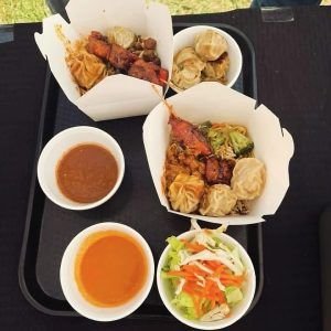 A tray of takeout food: dumplings, chicken, vegetables, and sauces in small bowls.