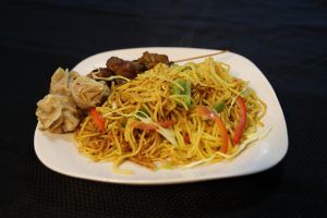 Plate of Chinese food: noodles, dumplings, meat skewers, with vegetables.