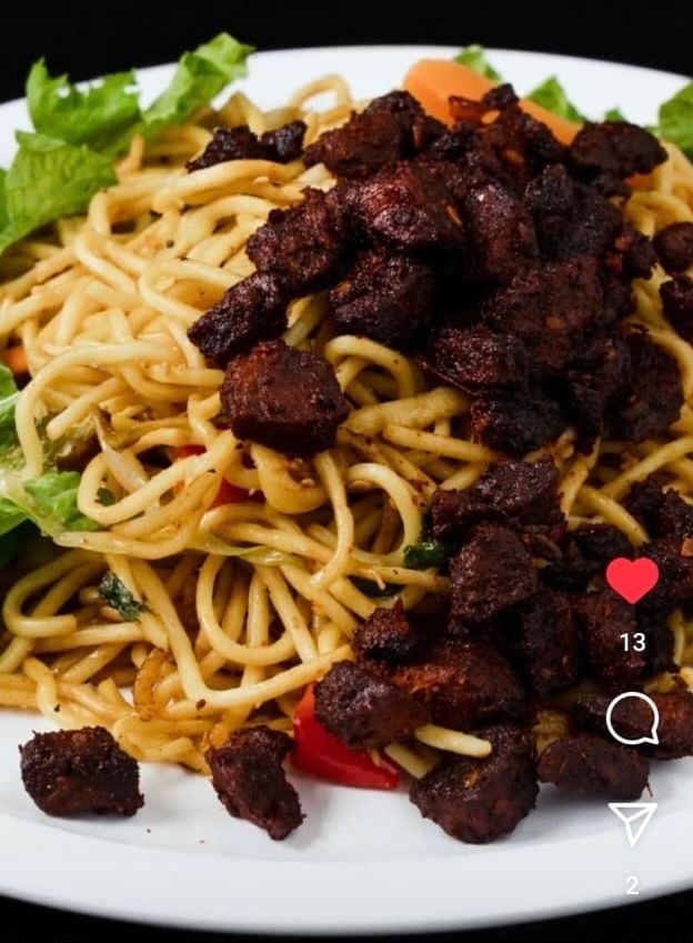Noodles topped with dark meat and lettuce on a white plate.