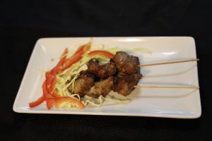Skewered meat on white plate with red peppers and cabbage.
