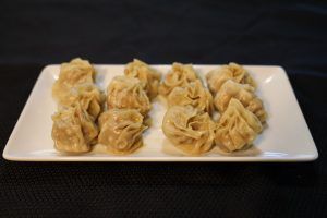 Steamed dumplings arranged on a white rectangular plate, against a dark background.