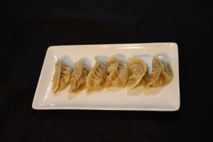 Dumplings on a white rectangular plate against a black background.