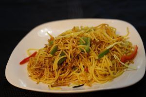 Yellow noodles with mixed vegetables on a white plate.