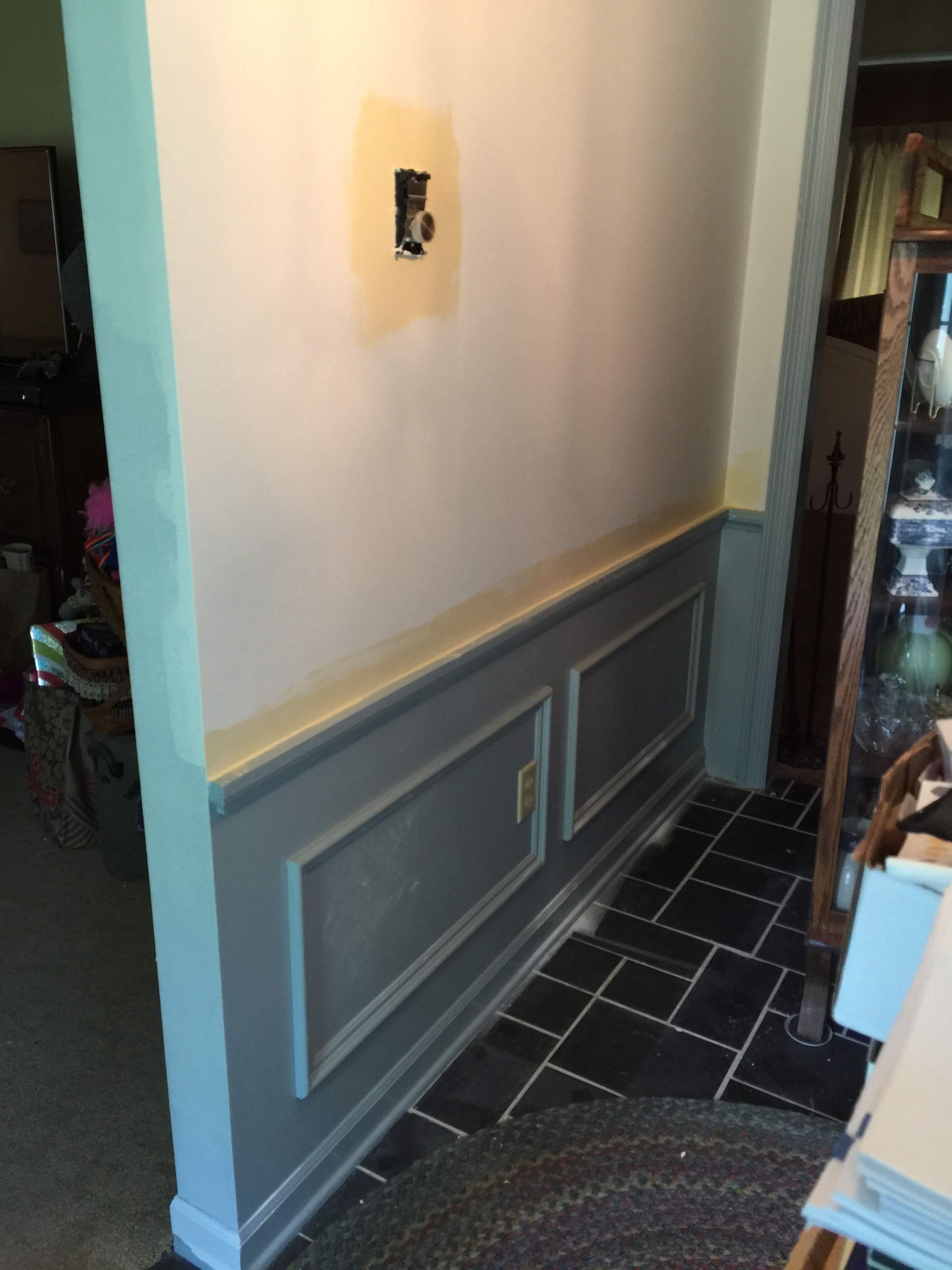 Wainscoting and wall painted gray and light green.  Black tile floor. Electrical outlet visible.