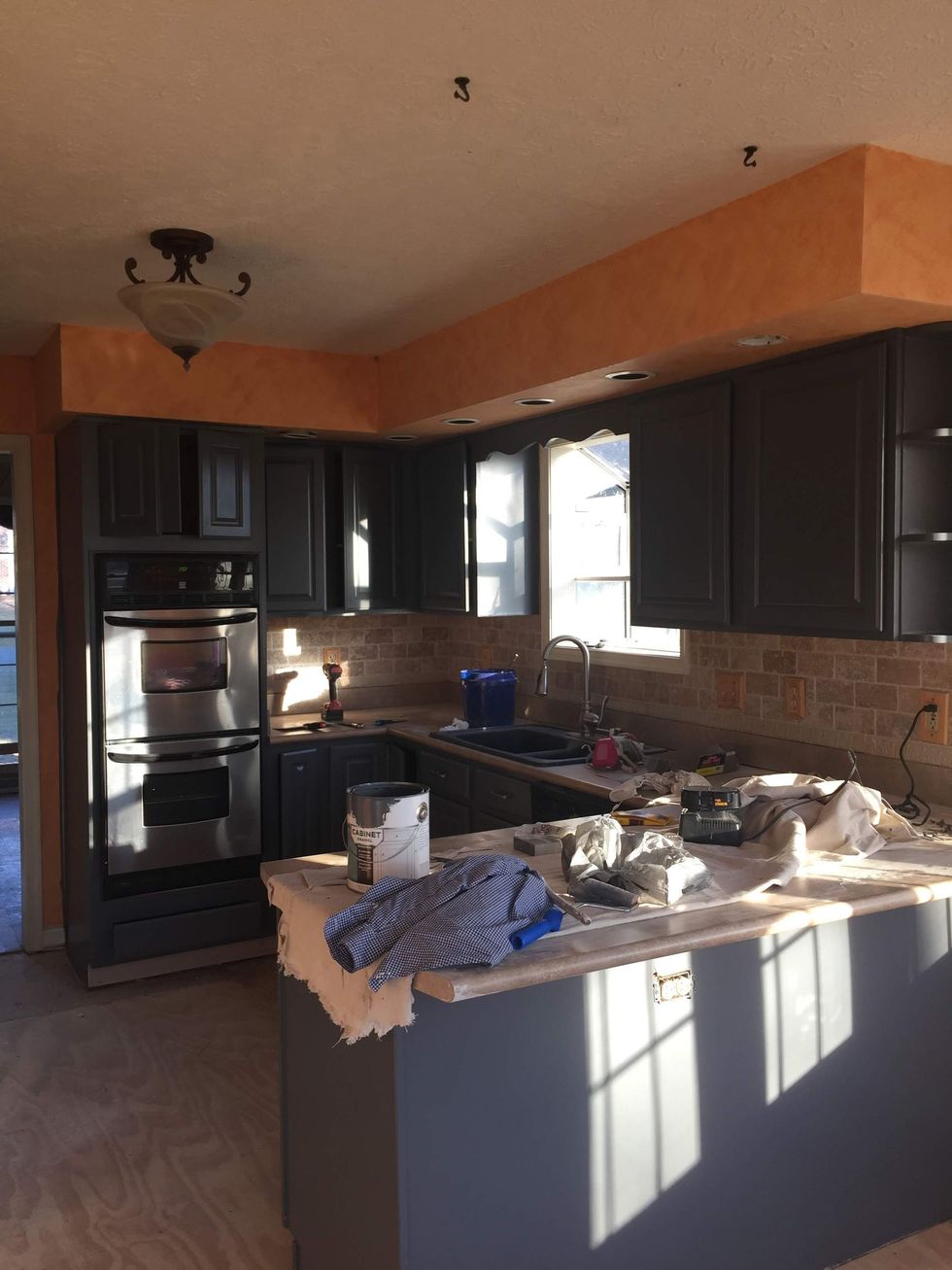 Kitchen with dark gray cabinets, orange upper wall, brick backsplash, and a light-colored island.