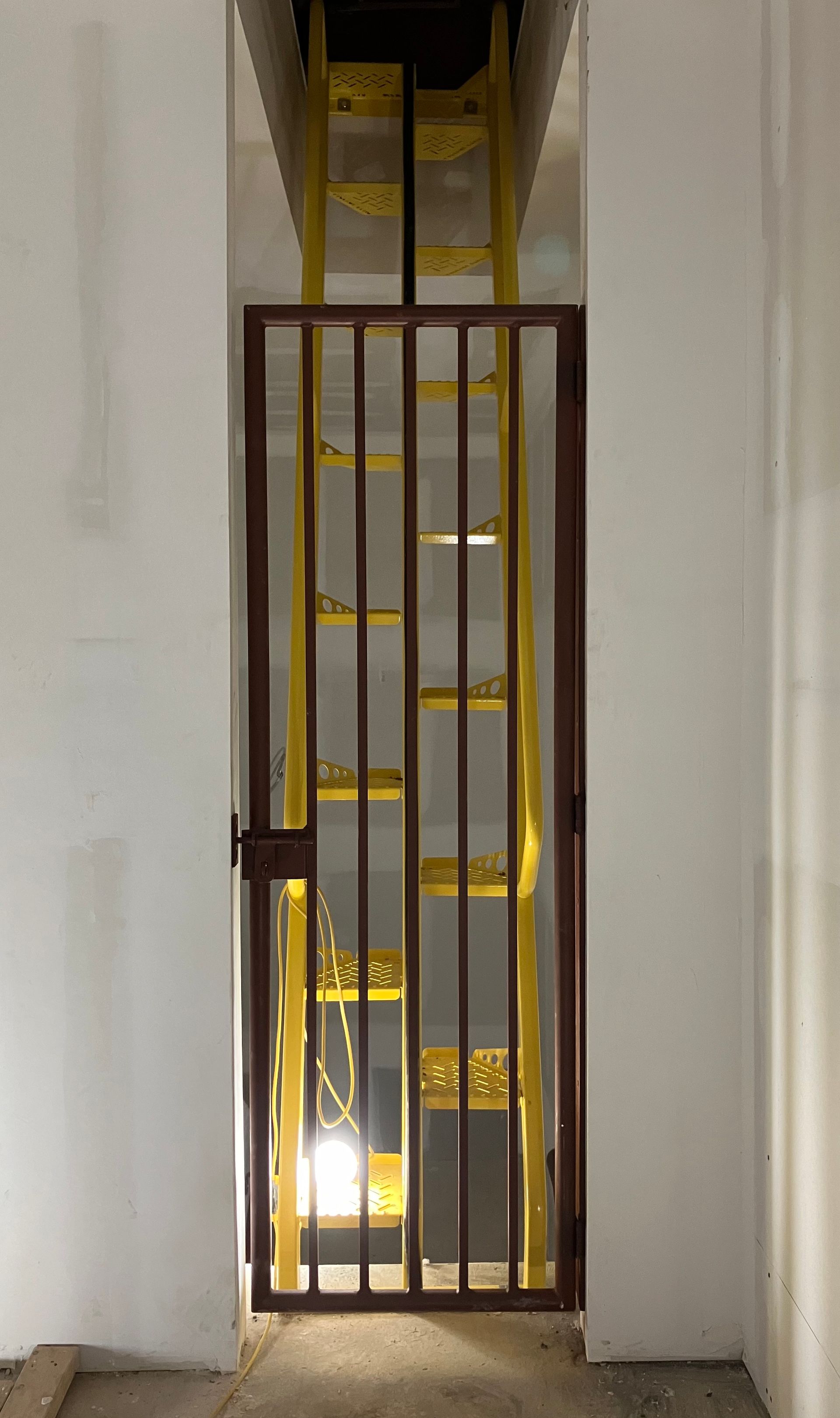A yellow ladder is behind a metal gate in a building.