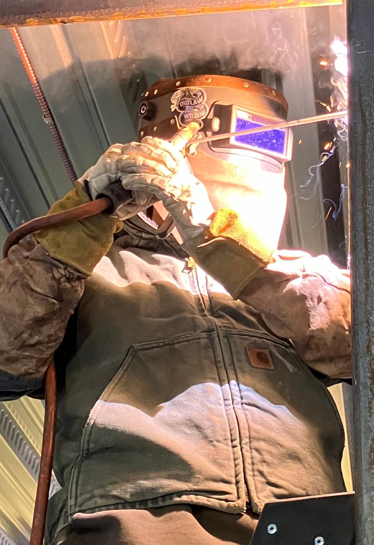 A man wearing a welding mask is welding a piece of metal.