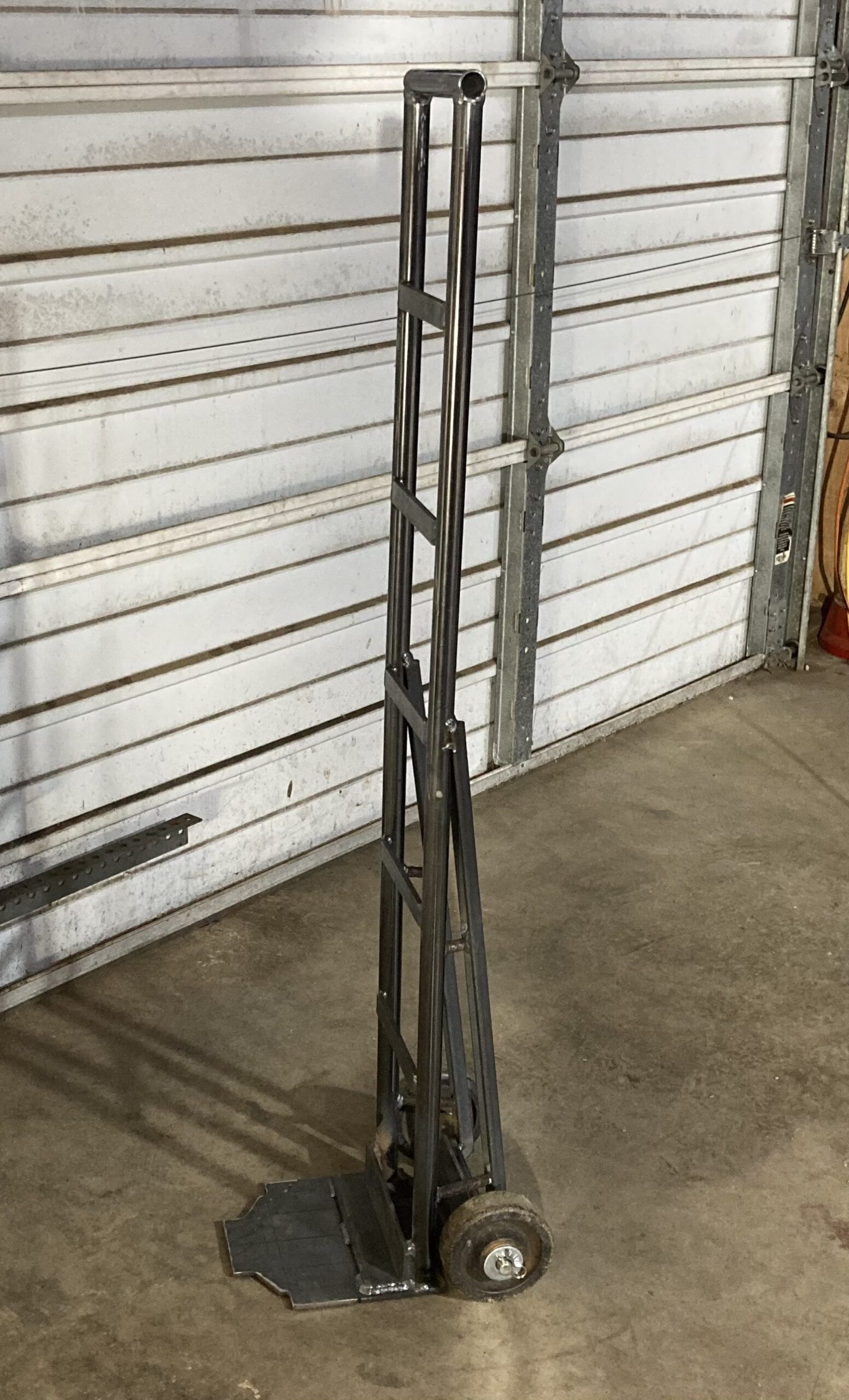 A hand truck is sitting in front of a garage door.