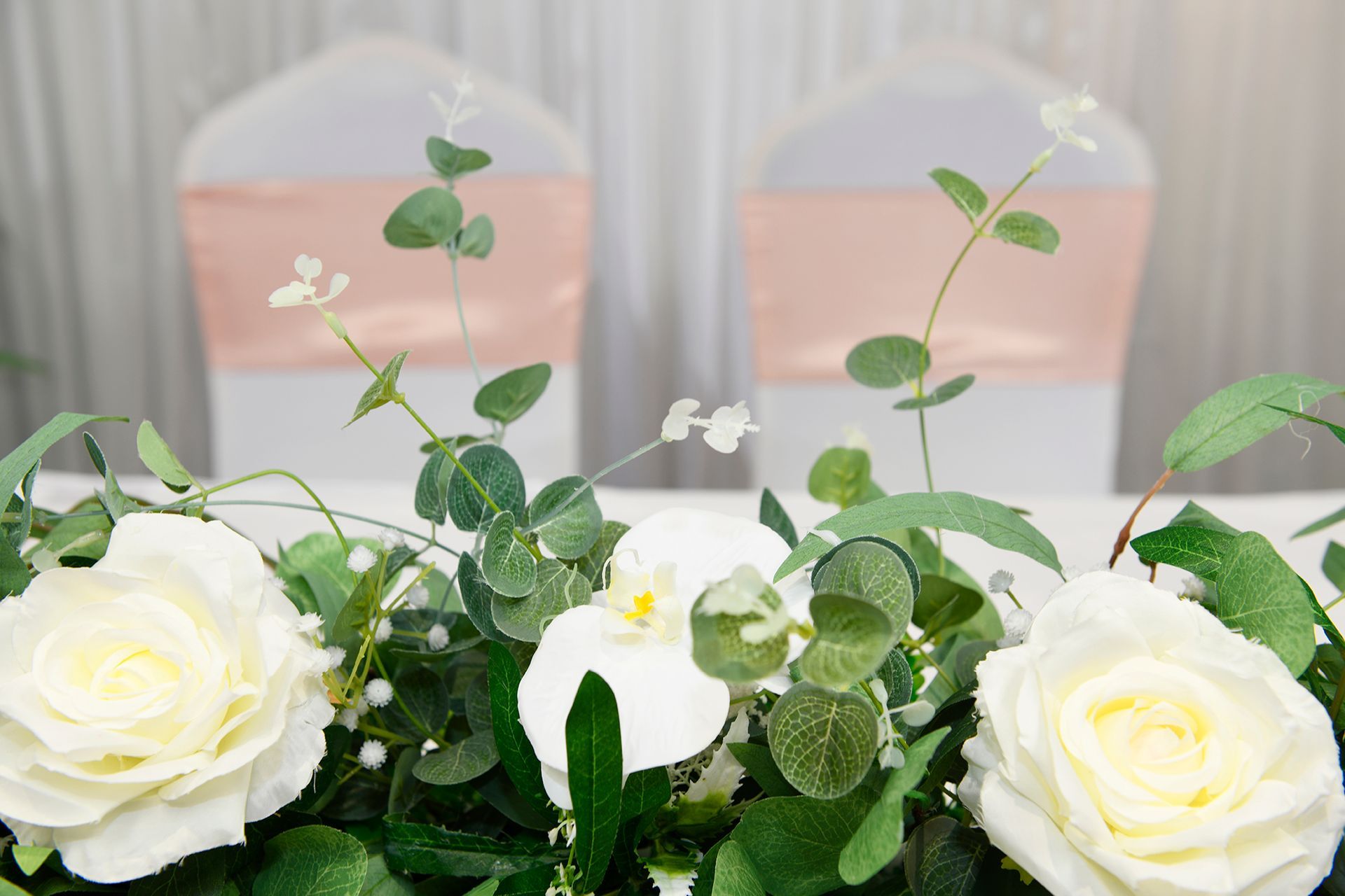 A table with white roses and greenery on it.