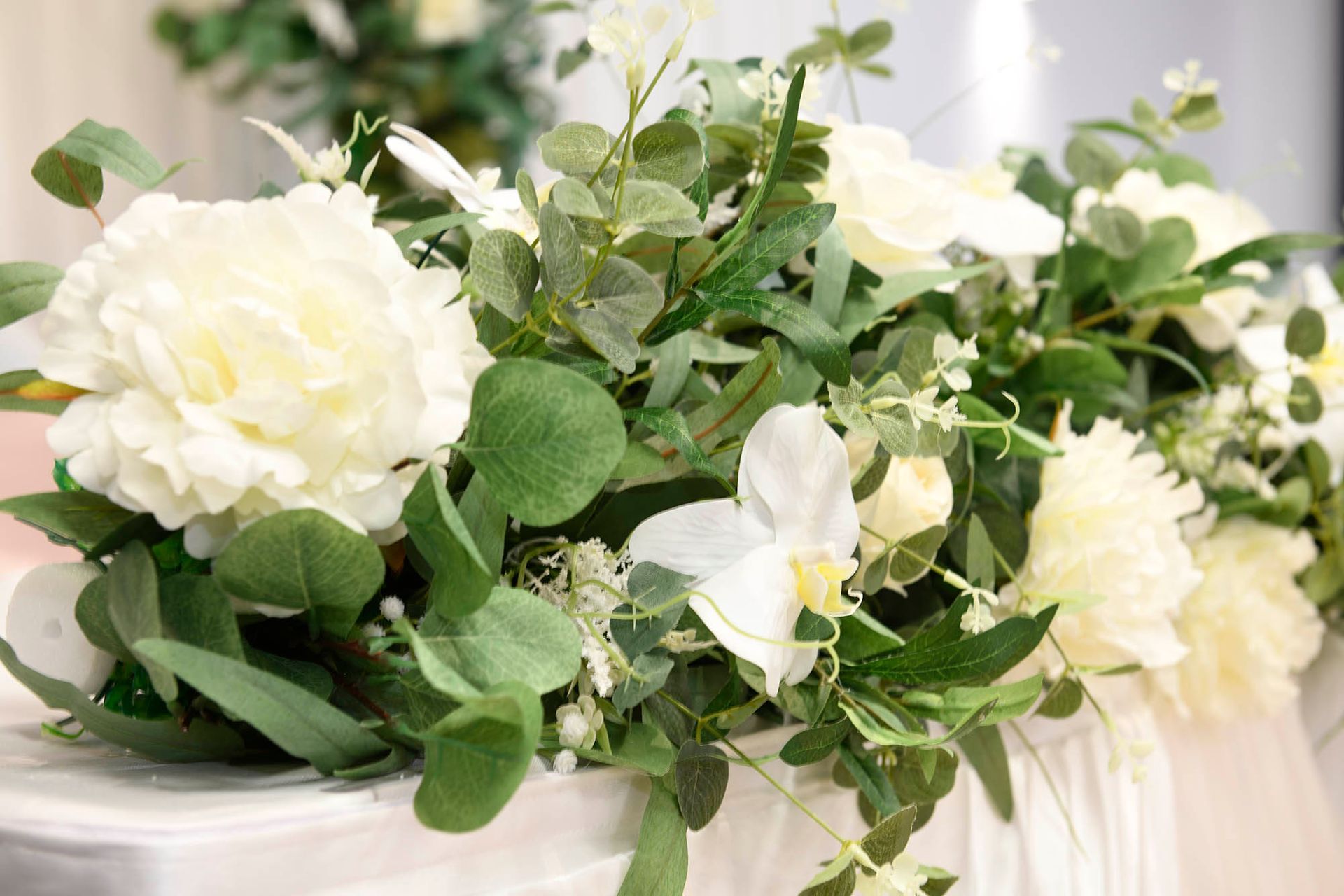 A vase filled with white flowers and green leaves on a table.