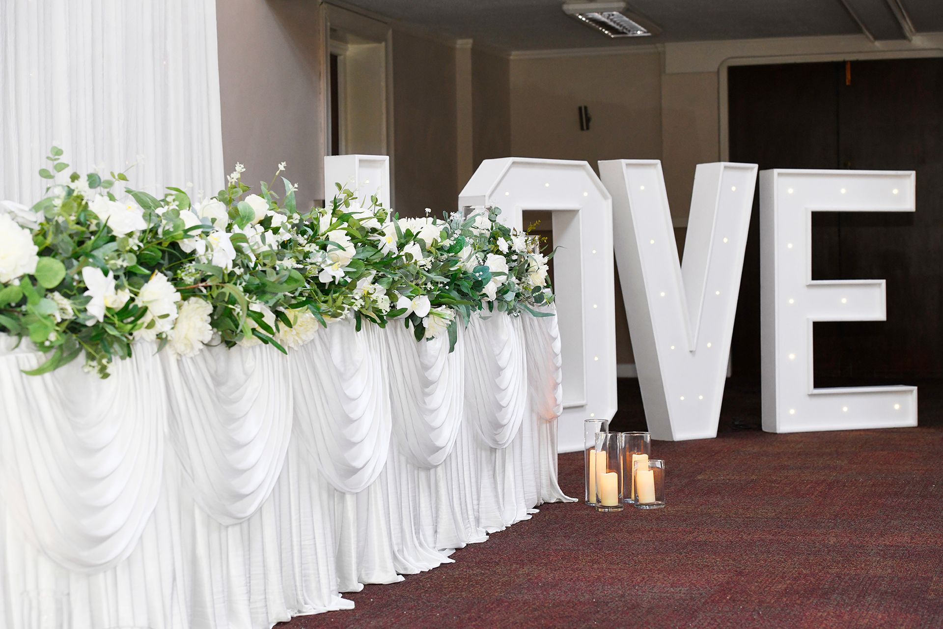 A large white love sign is sitting next to a table with flowers and candles.