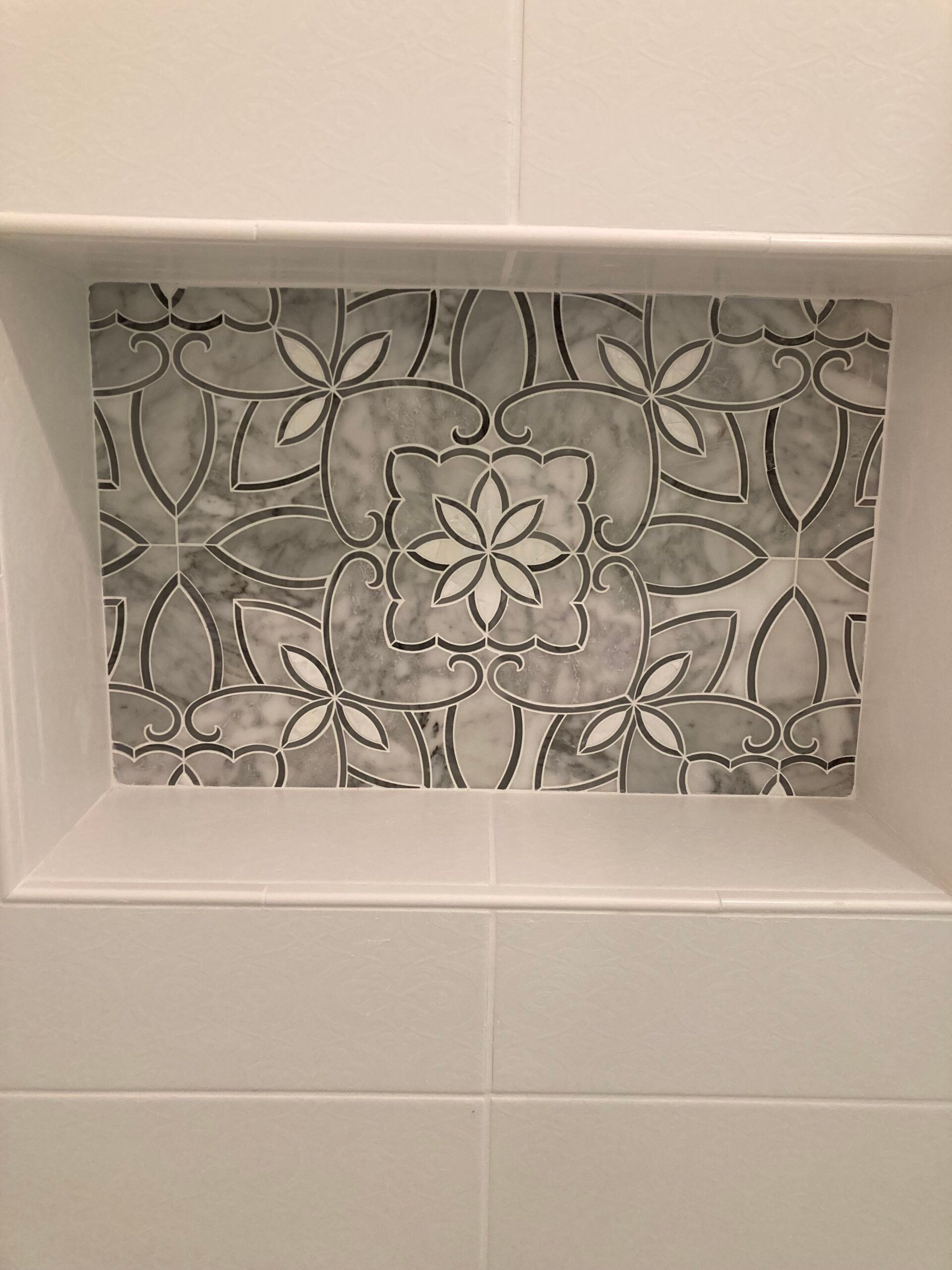 Recessed shelf with floral mosaic tile design, surrounded by white rectangular tiles.