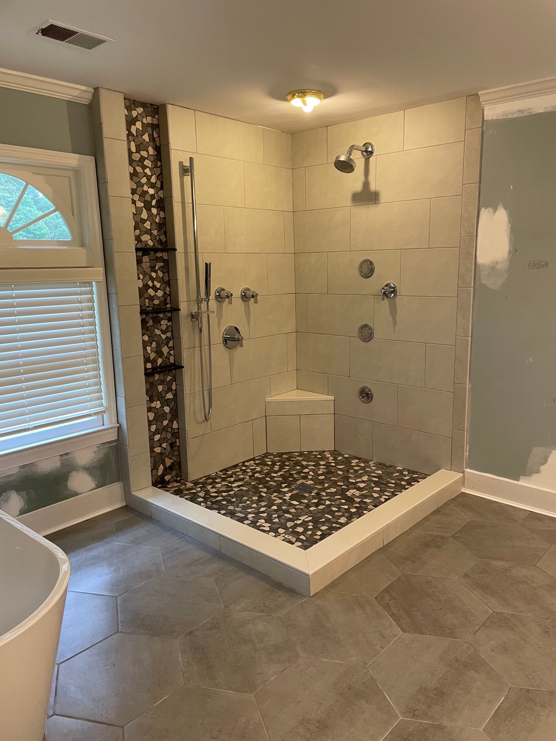 Shower with stone floor, pebble base. Beige tiled walls, chrome fixtures.