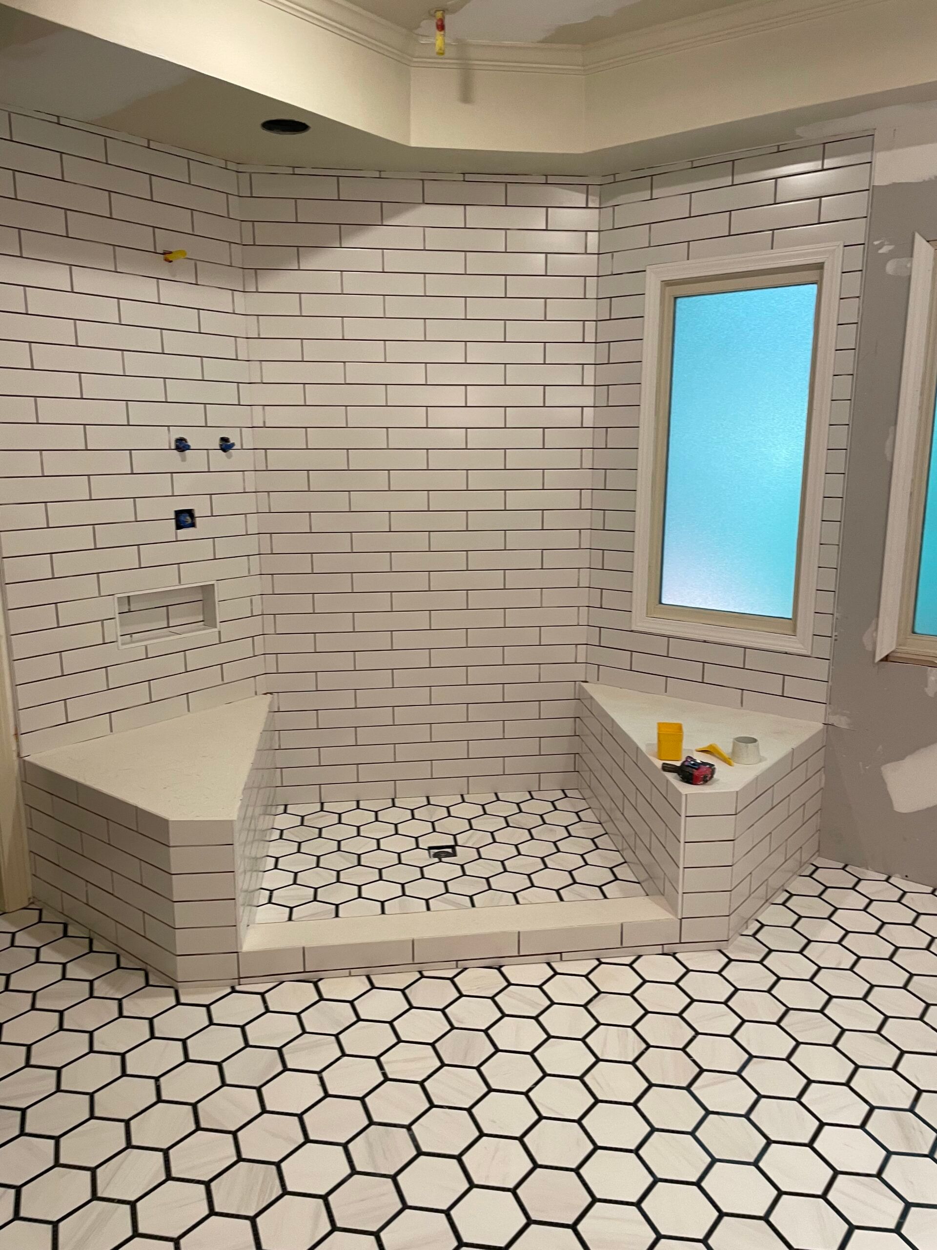 Bathroom under construction with white tile, a shower, and hexagon floor tile.