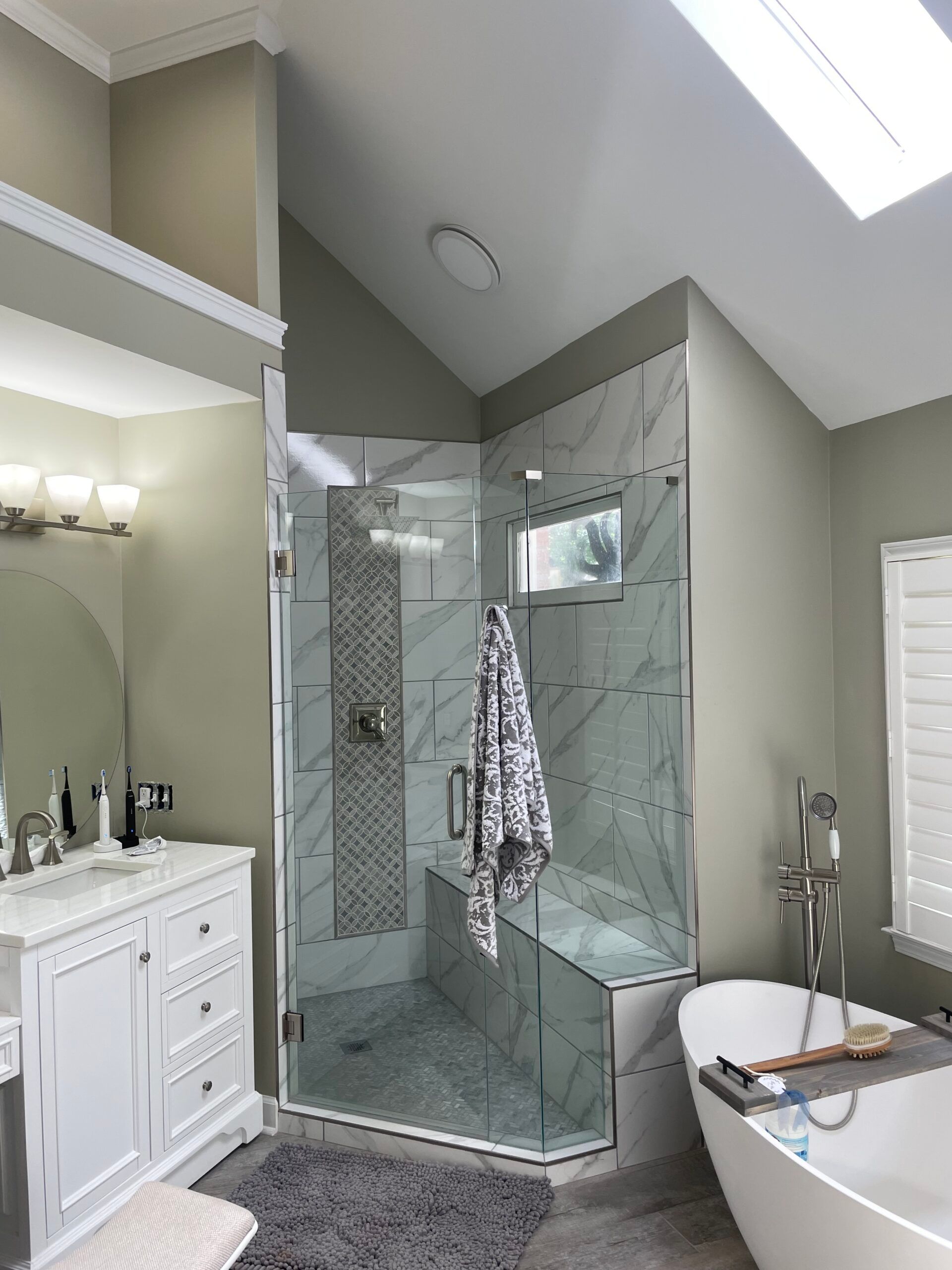 Bathroom with glass shower, white tub, vanity, and light green walls.