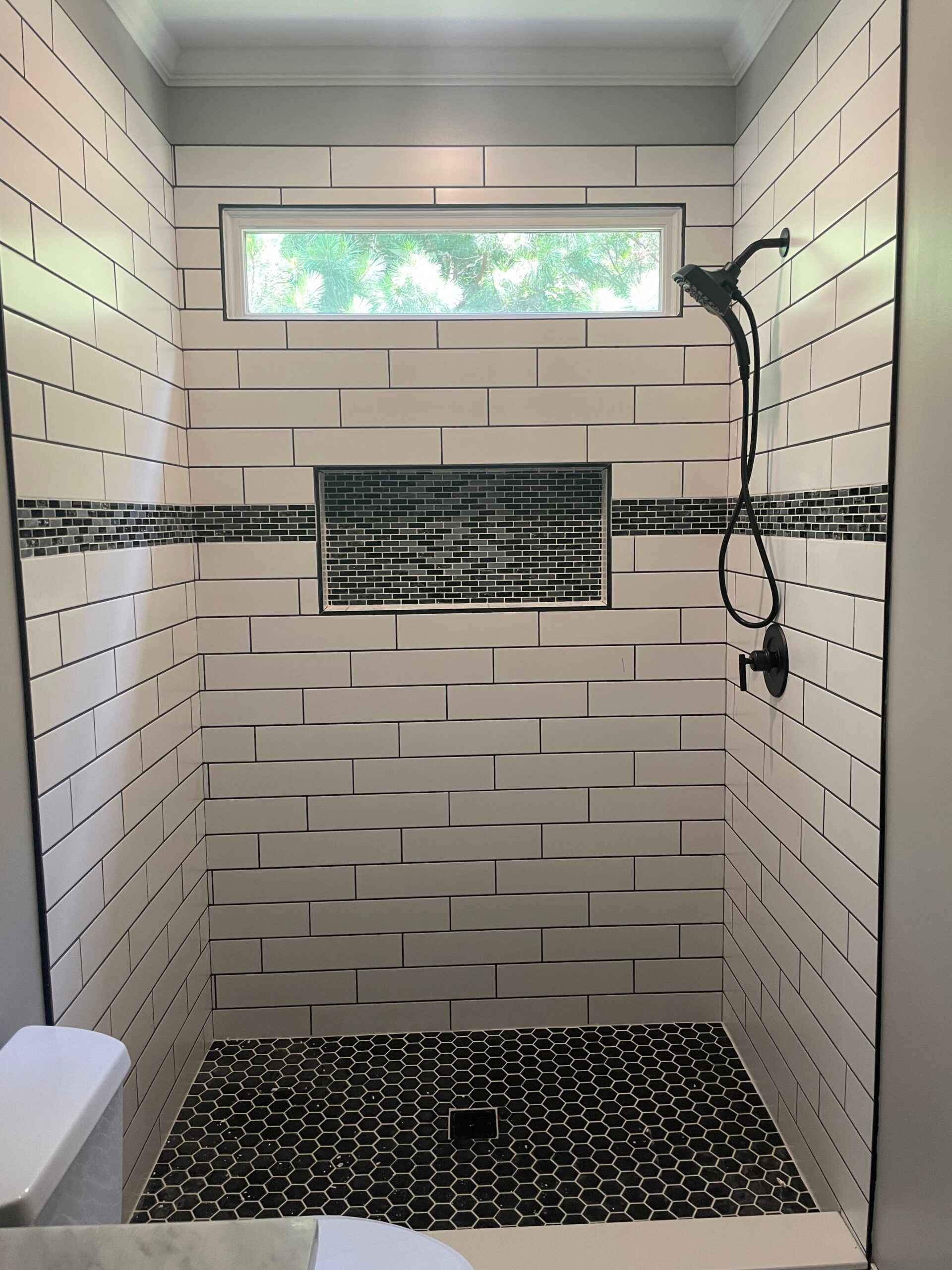 Shower with white textured tile walls, black pebble floor, and a black shower head.