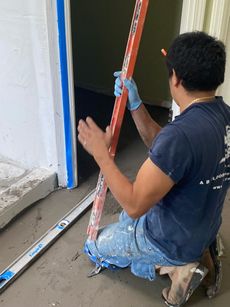 Person using a level to check flooring. The person kneels inside a doorway, holding the level.