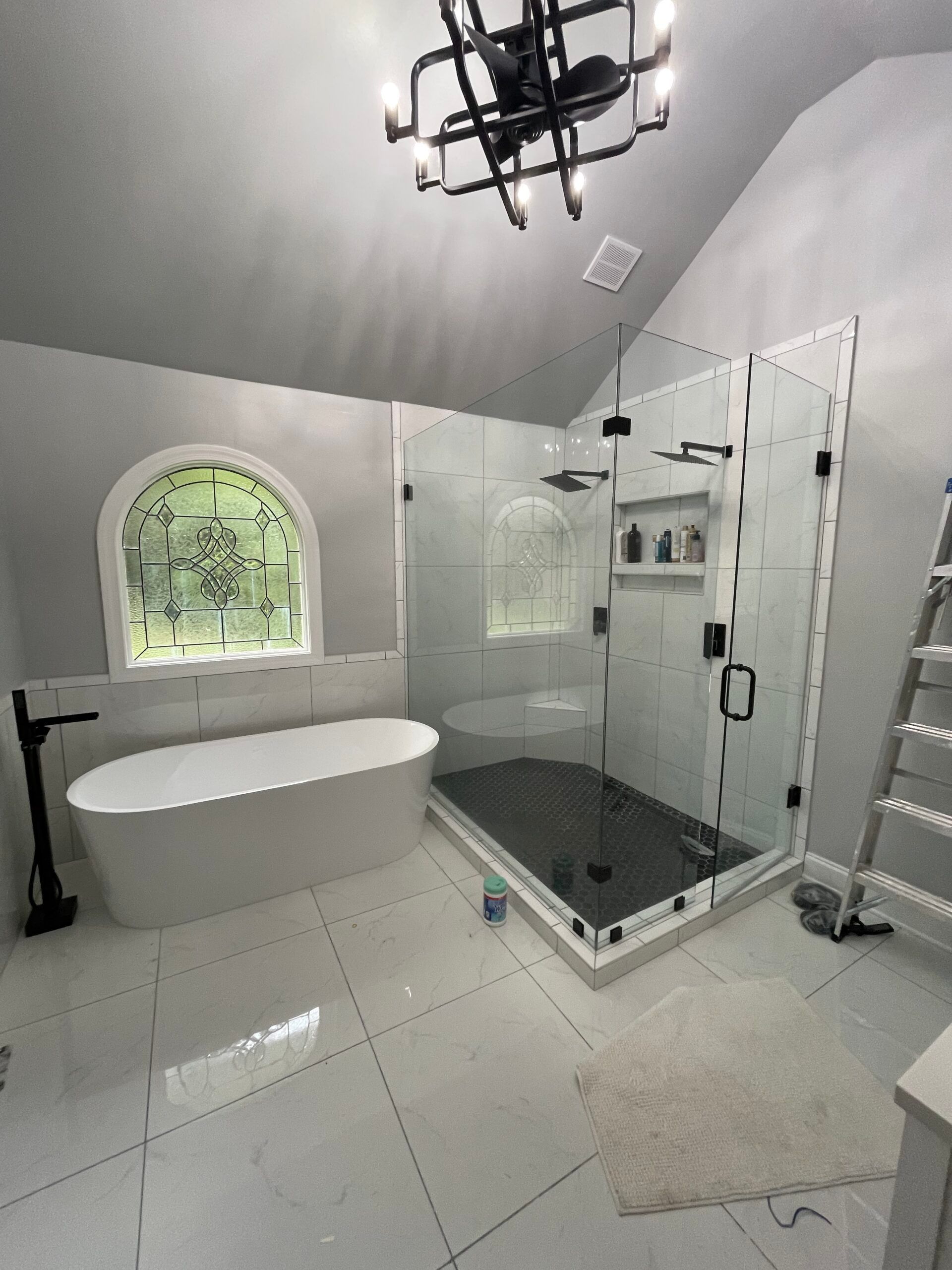 Spacious bathroom with white tile floor, a large glass shower, and freestanding tub. Gray walls and vaulted ceiling.