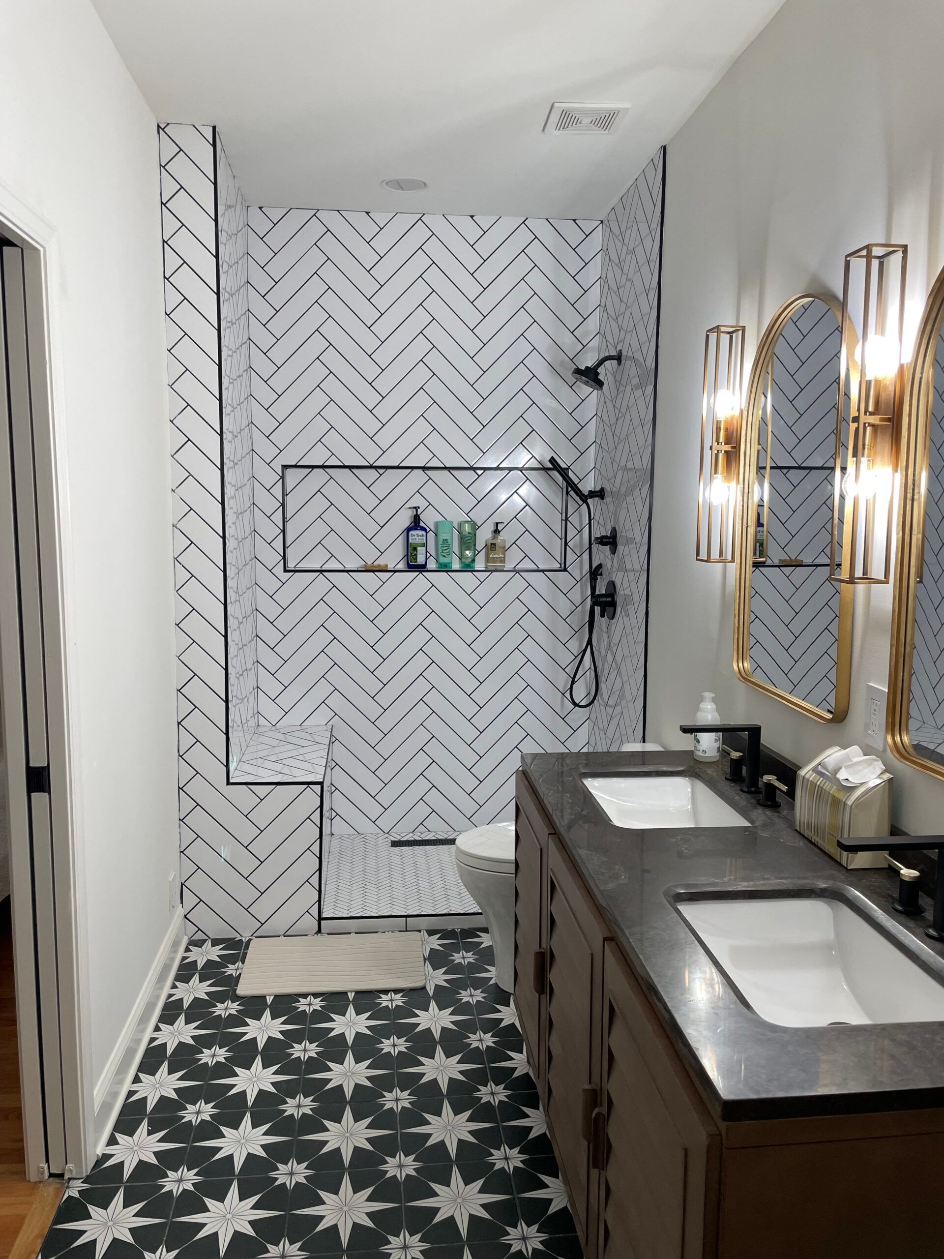 Modern bathroom with patterned black and white tiles, double vanity, and a walk-in shower.