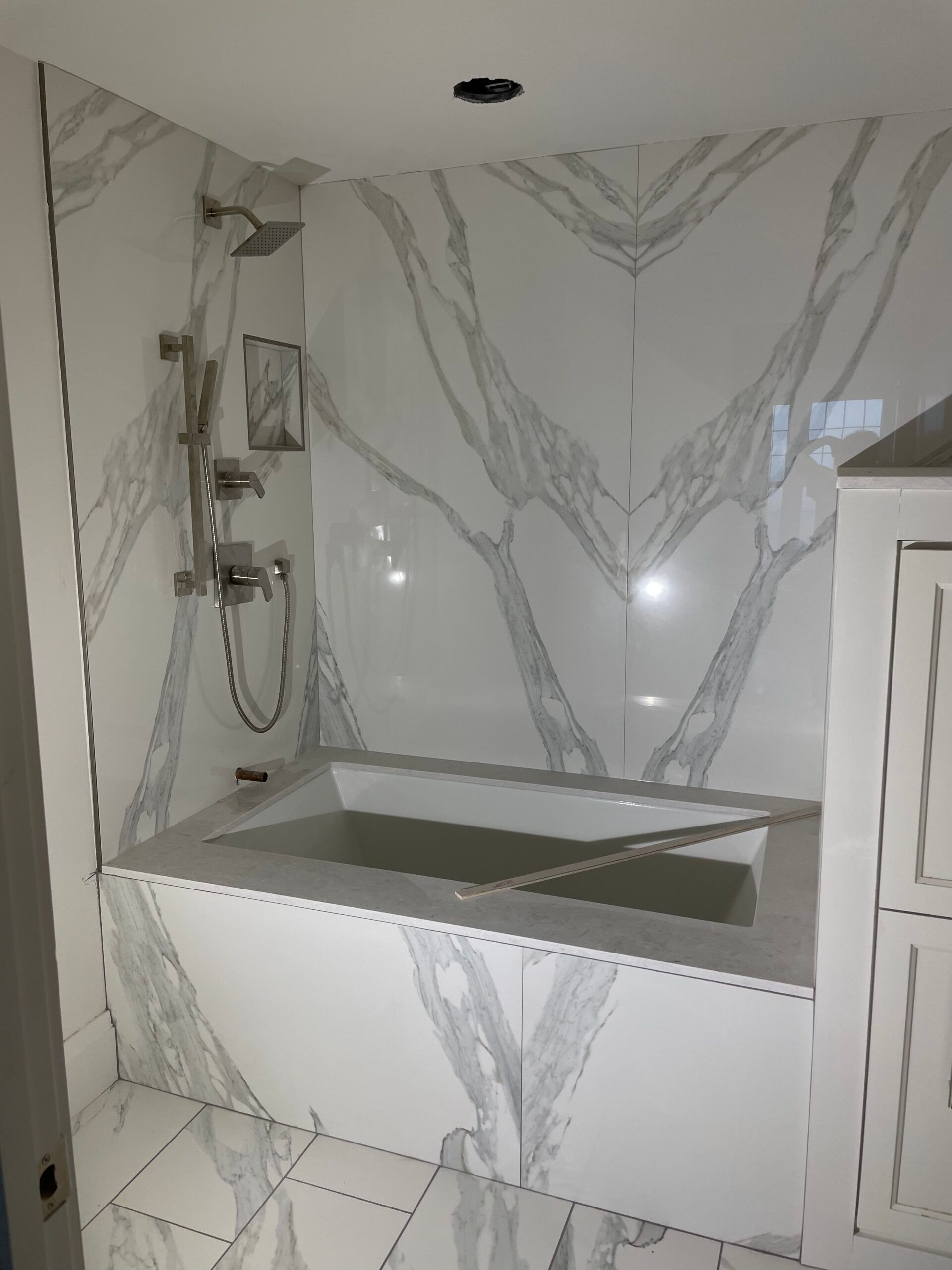 Bathroom with marble-patterned tile, a built-in tub, and a shower fixture.