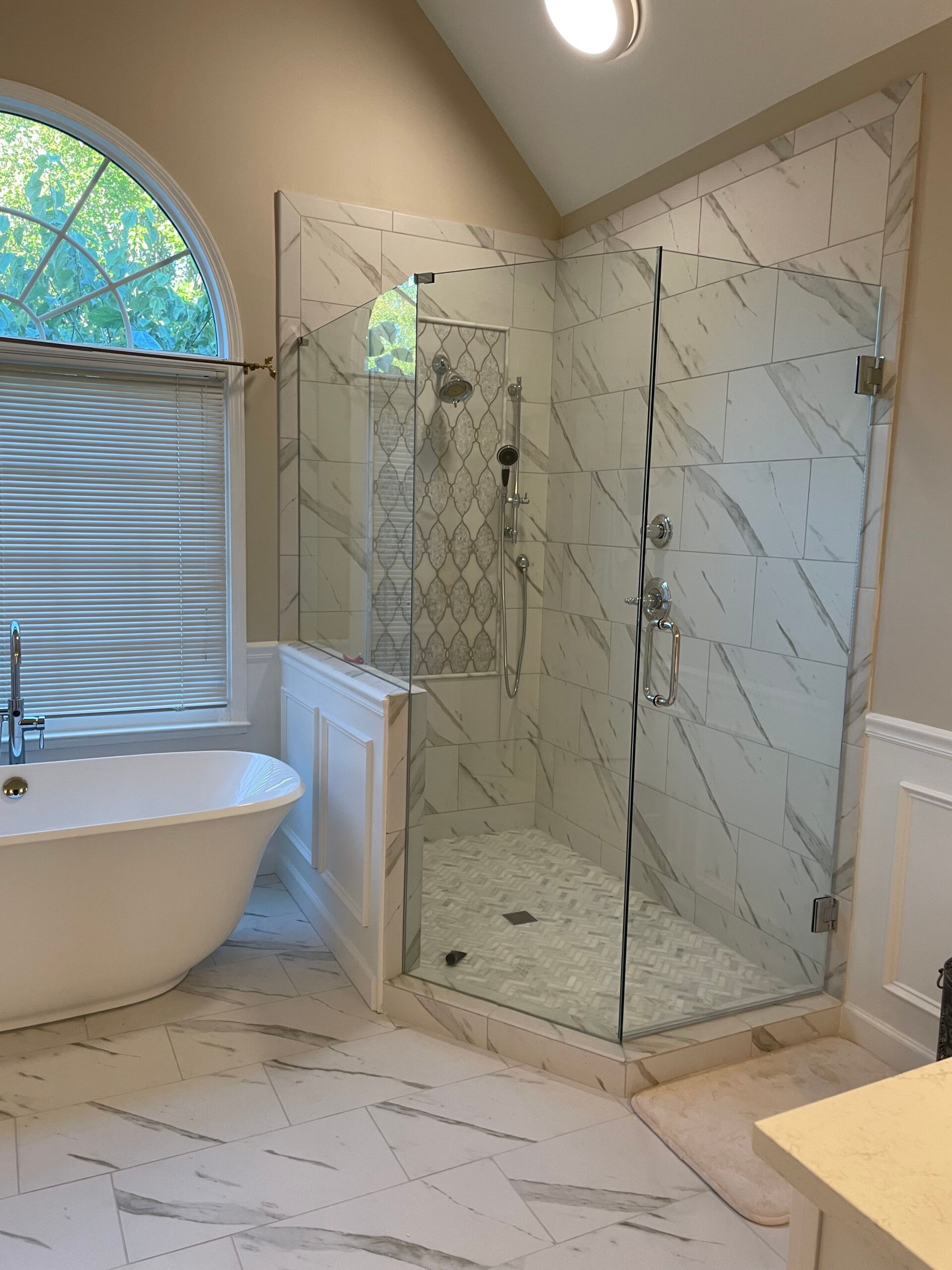 Bathroom with large marble-tiled walk-in shower, freestanding tub, and a window with blinds.