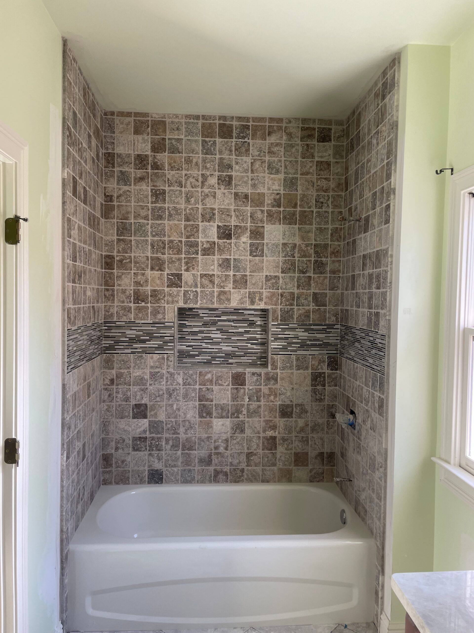 Tiled bathtub surround with a built-in niche. Features brown, tan, and gray tiles.