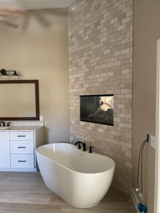 Bathroom with a white freestanding tub, brick accent wall, built-in fireplace, and vanity with mirror.