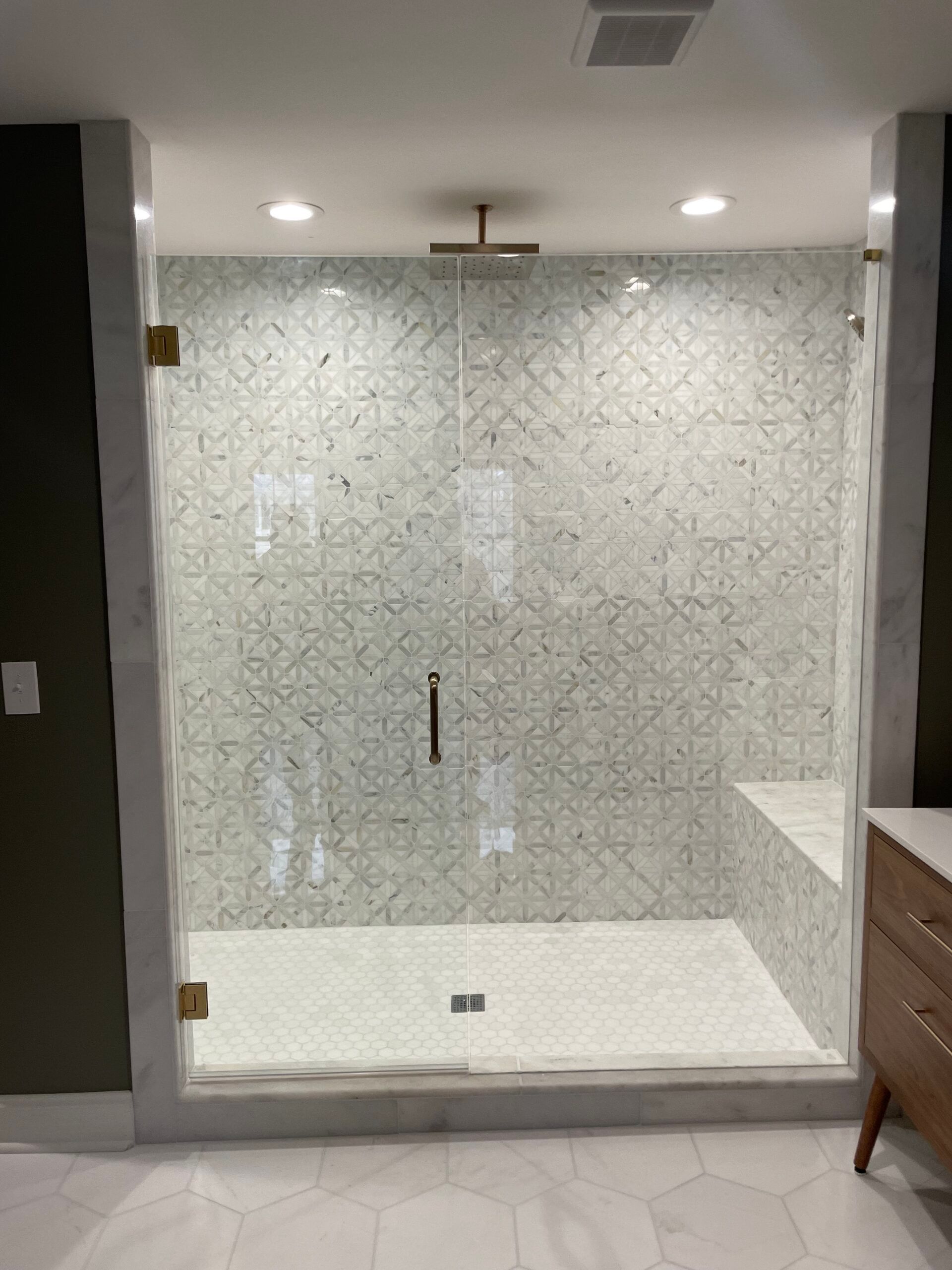 Glass shower with white patterned tile walls and floor, gold hardware.