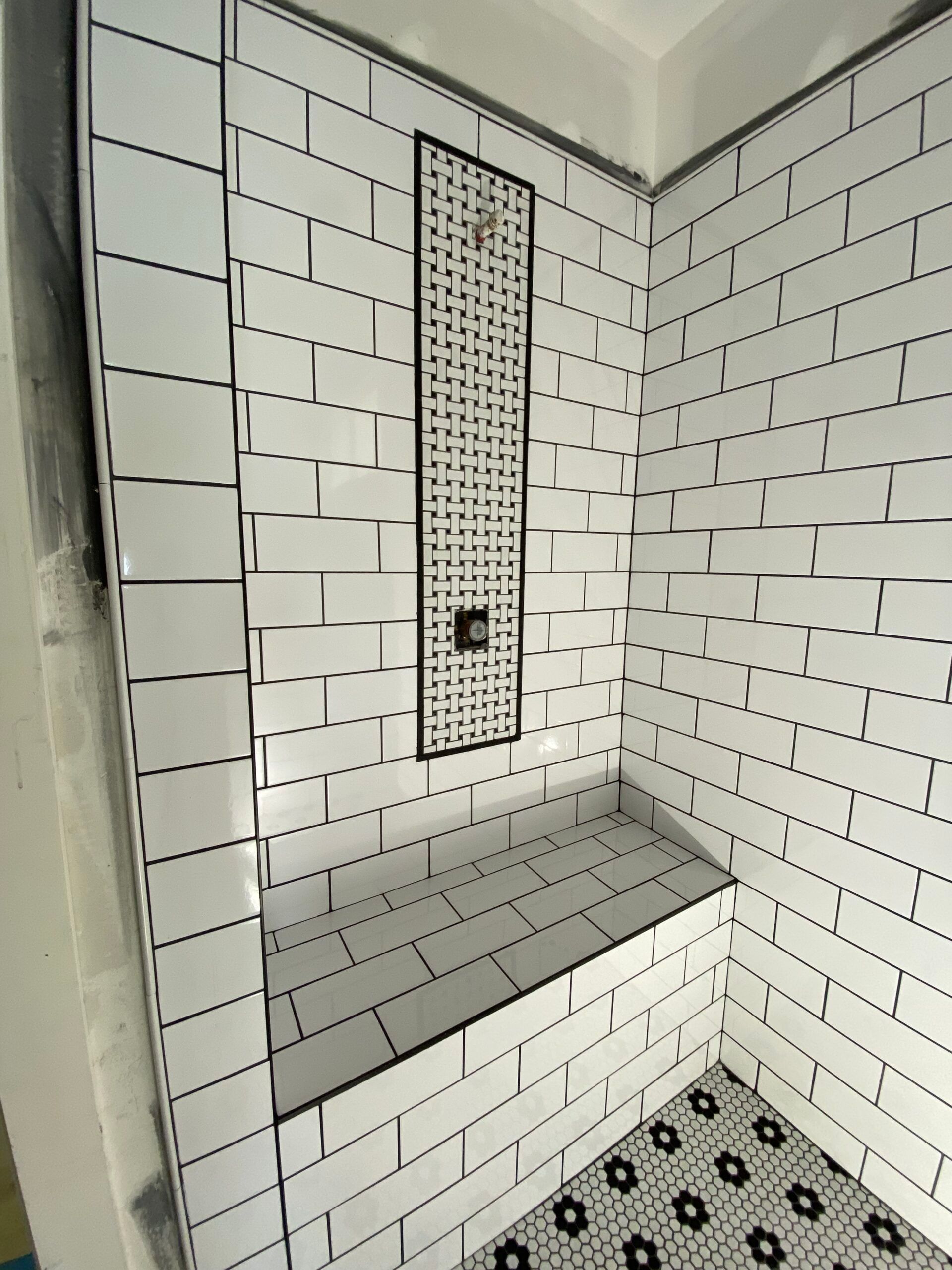 Tiled shower with white subway tiles, a black accented shower niche, and a bench. The floor is patterned.