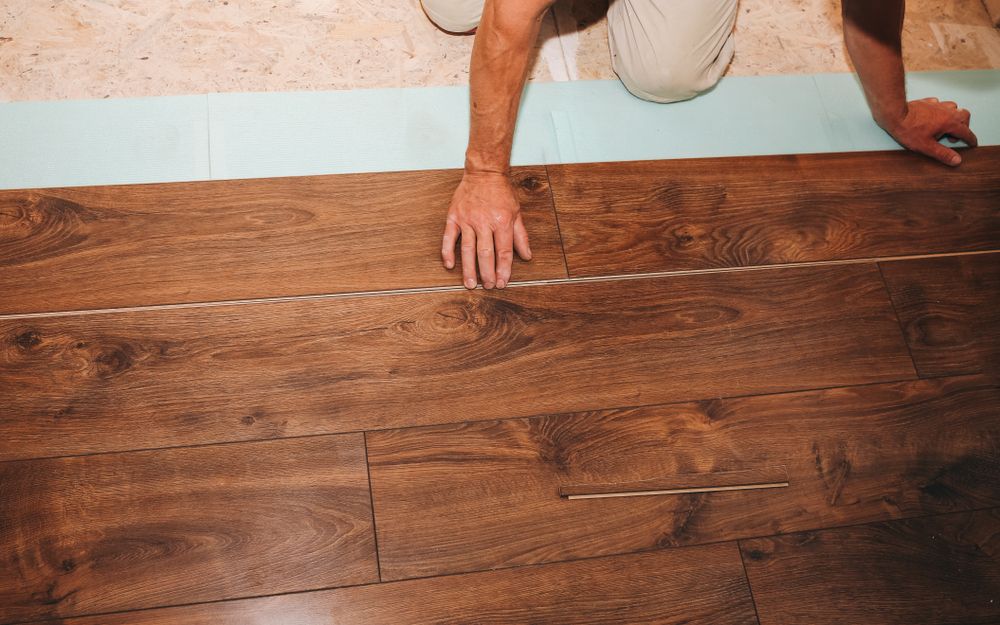 Person installing wood flooring, placing a plank with hands.