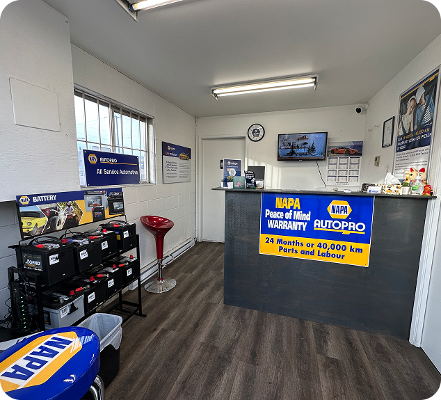 Interior of a NAPA AutoPro shop with a counter, batteries on display, and a small red stool.