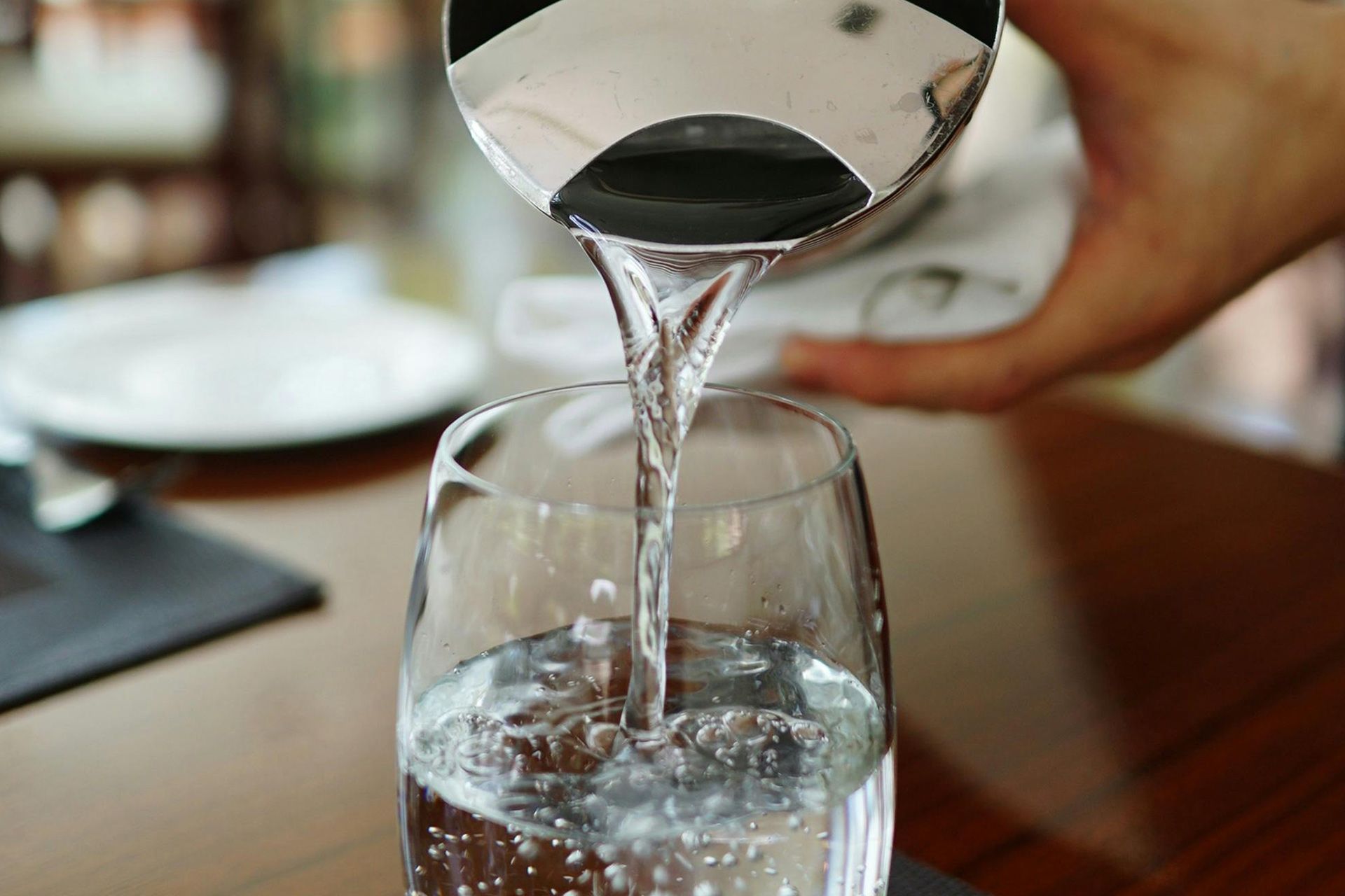 Water being poured from a silver pitcher into a clear glass, indoors.