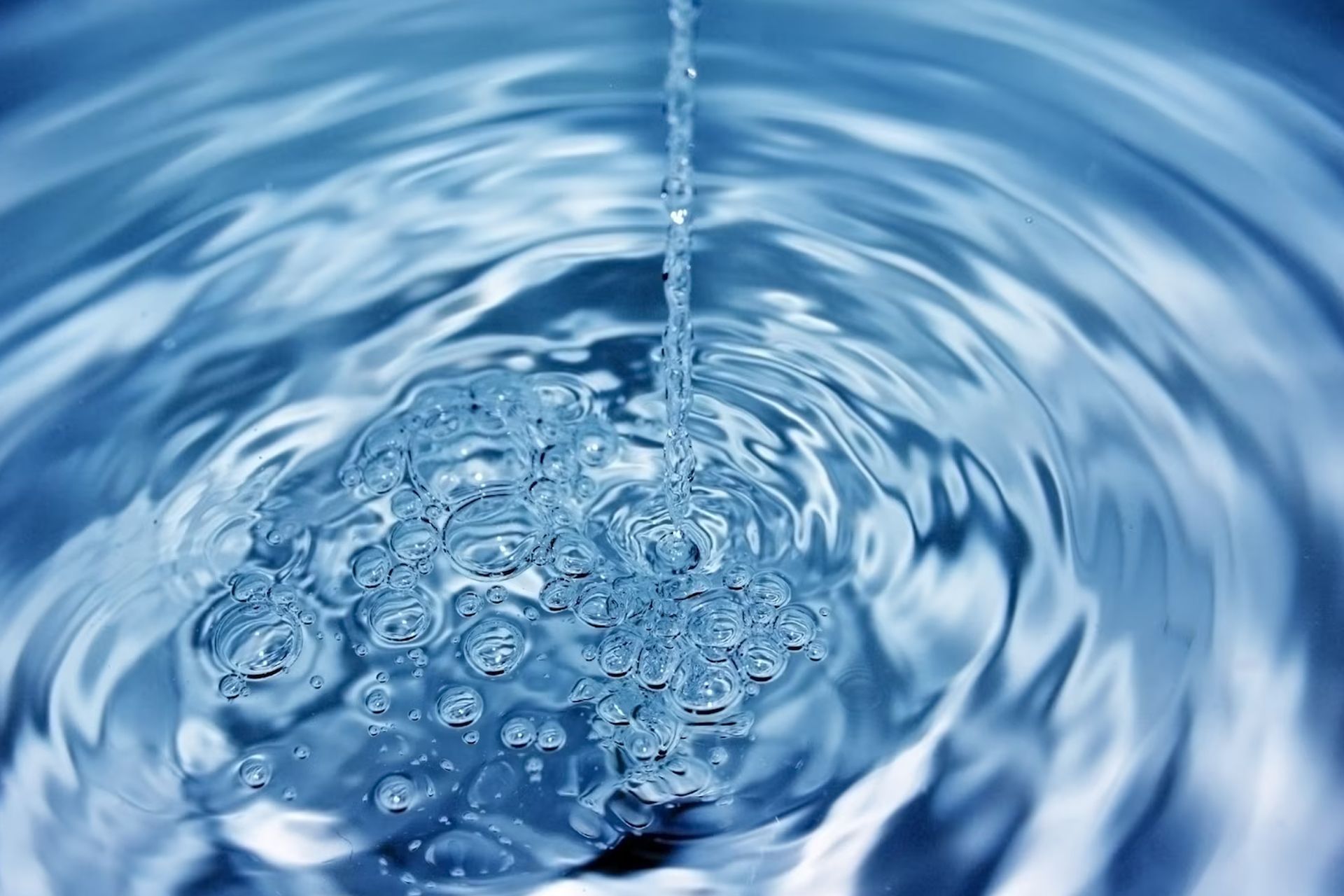 Water pouring, creating bubbles and concentric ripples in blue water.