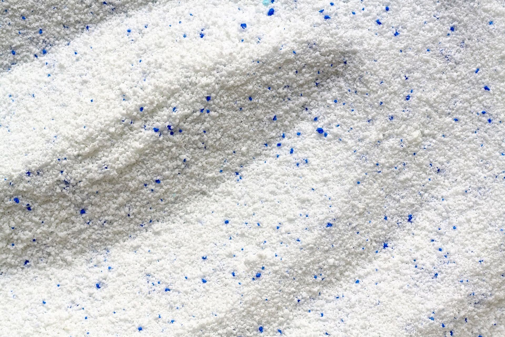 Close-up of white laundry detergent powder with scattered blue particles.
