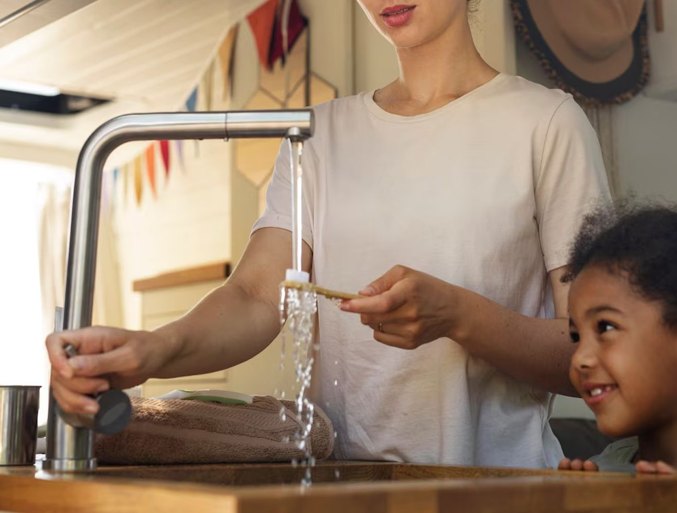 Woman and child at sink; woman rinses toothbrush with water, child watches smiling.