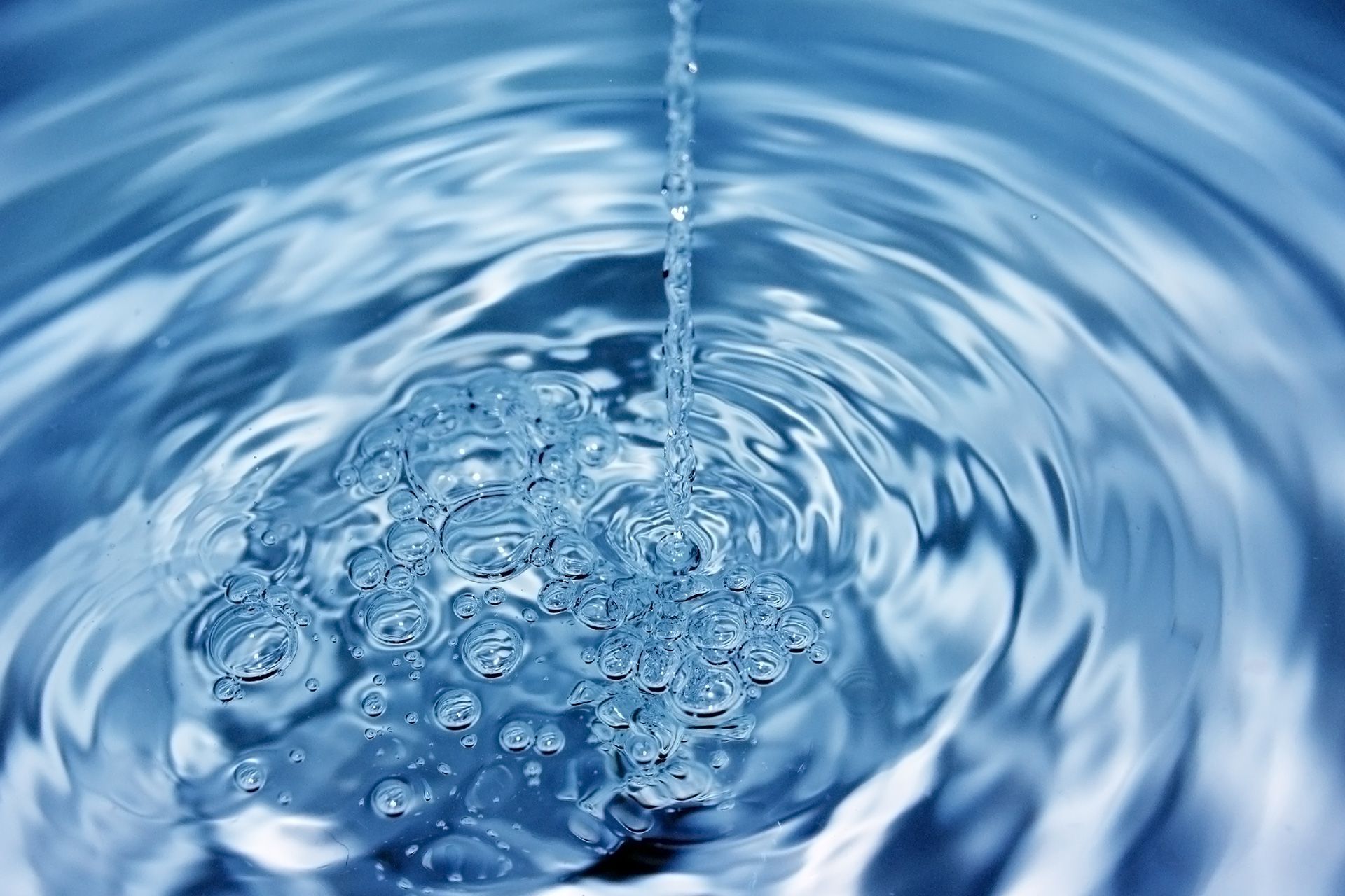 Water pouring, creating ripples and bubbles in a blue liquid.