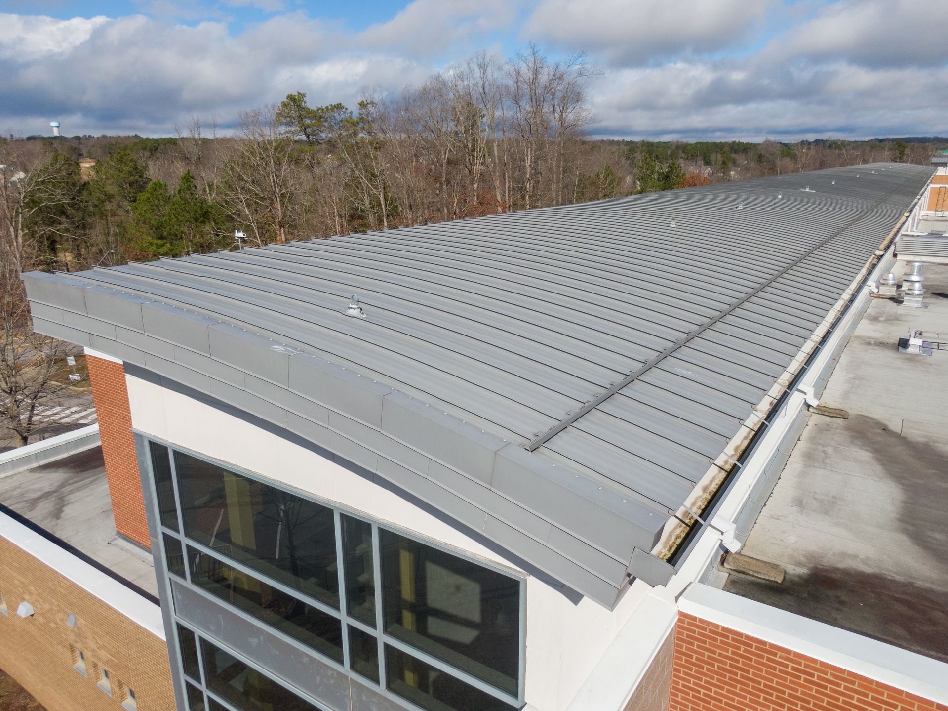 Gray metal roof on a building with large windows and brick facade, under a cloudy sky.